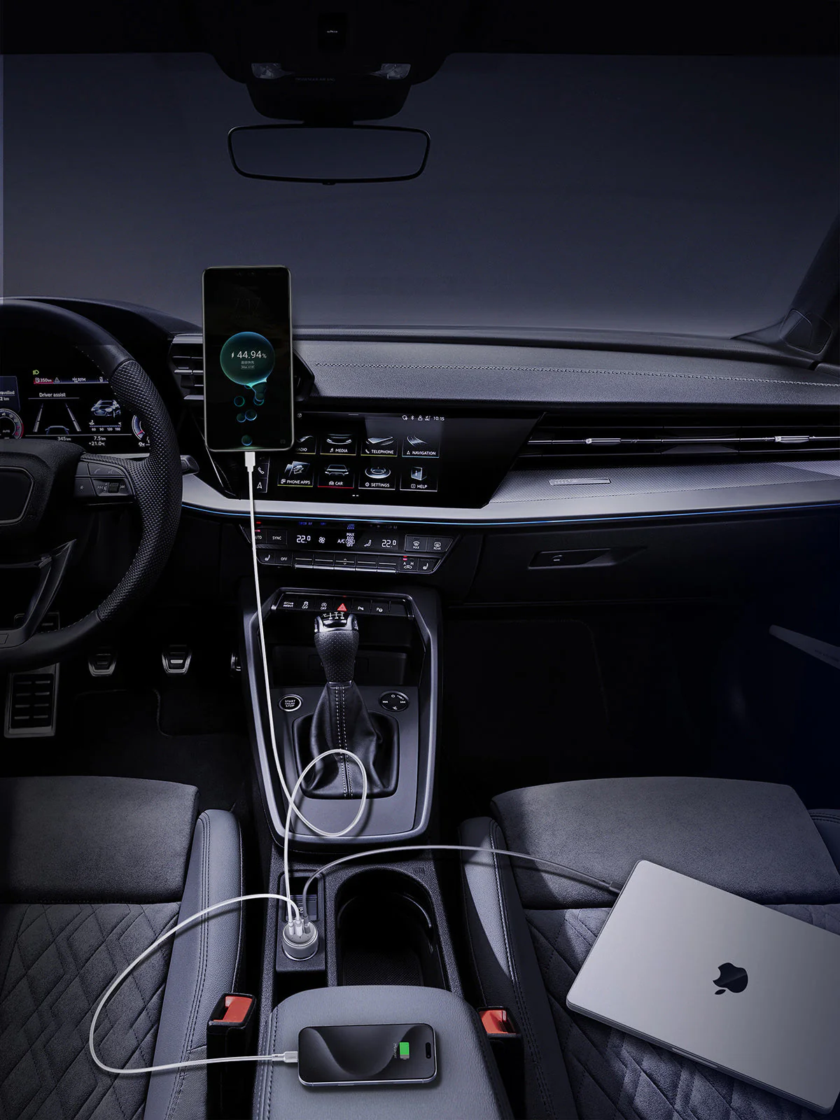 Interni auto con telefono in carica, percentuale batteria, laptop e cruscotto.