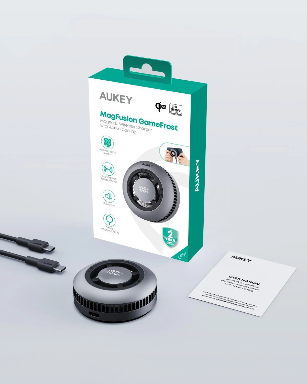Cargador inalámbrico gris Aukey MagFusion GameFrost, caja, cables y manual de usuario sobre fondo blanco.