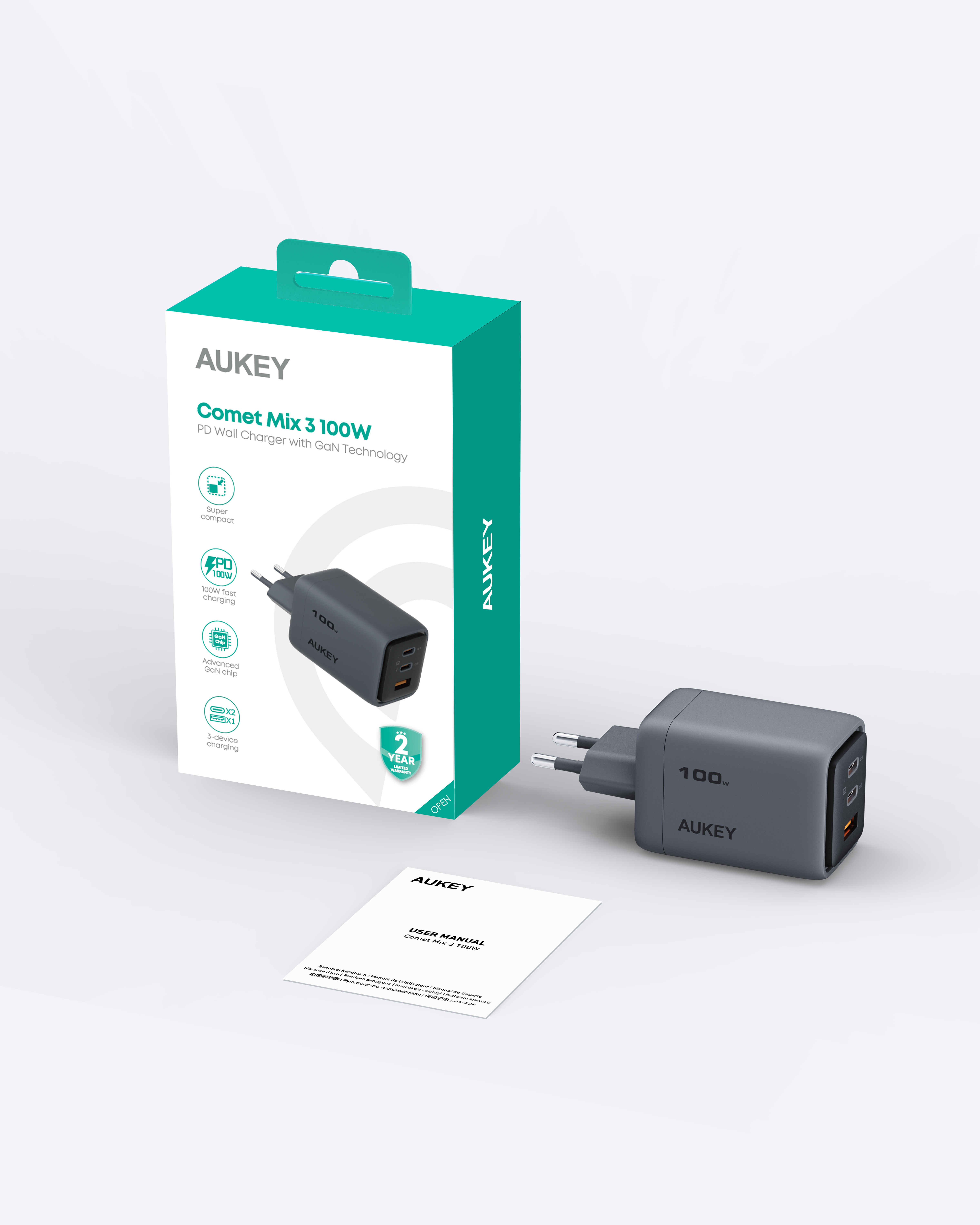 Un cargador AUKEY Comet Mix 3 100W con su caja y manual de usuario. El cargador es gris y la caja es verde azulado.
