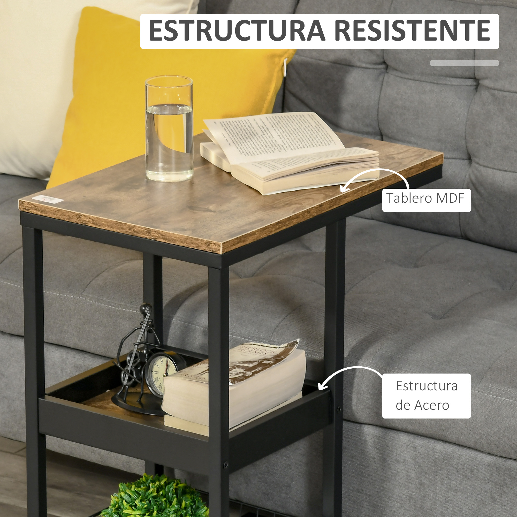 Una mesa auxiliar con un vaso de agua, libros y un reloj. Tiene una tapa de madera y estructura de metal negro. Un cojín amarillo en el fondo.