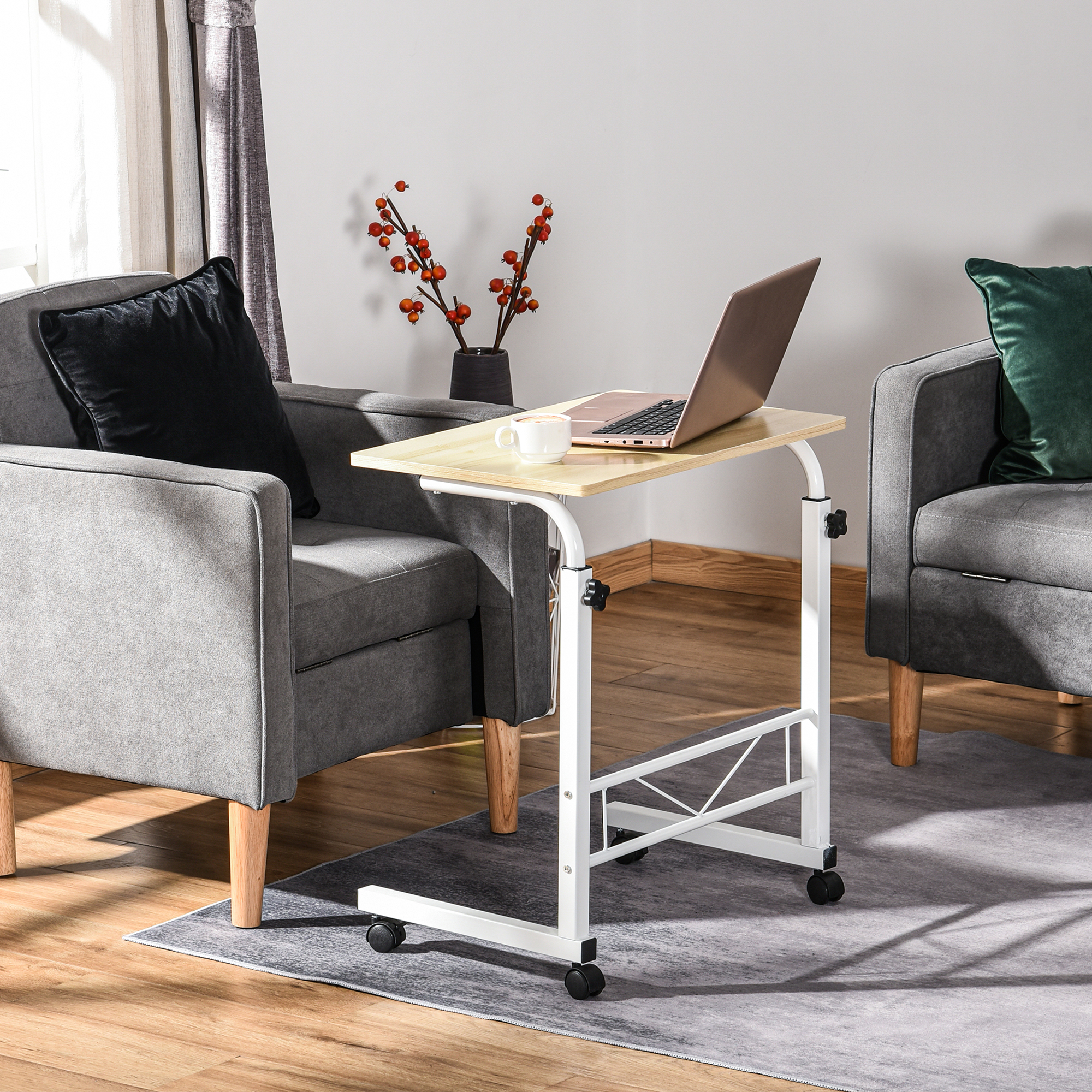 Un portátil sobre una mesa rodante entre dos sillones grises. Una taza en la mesa.