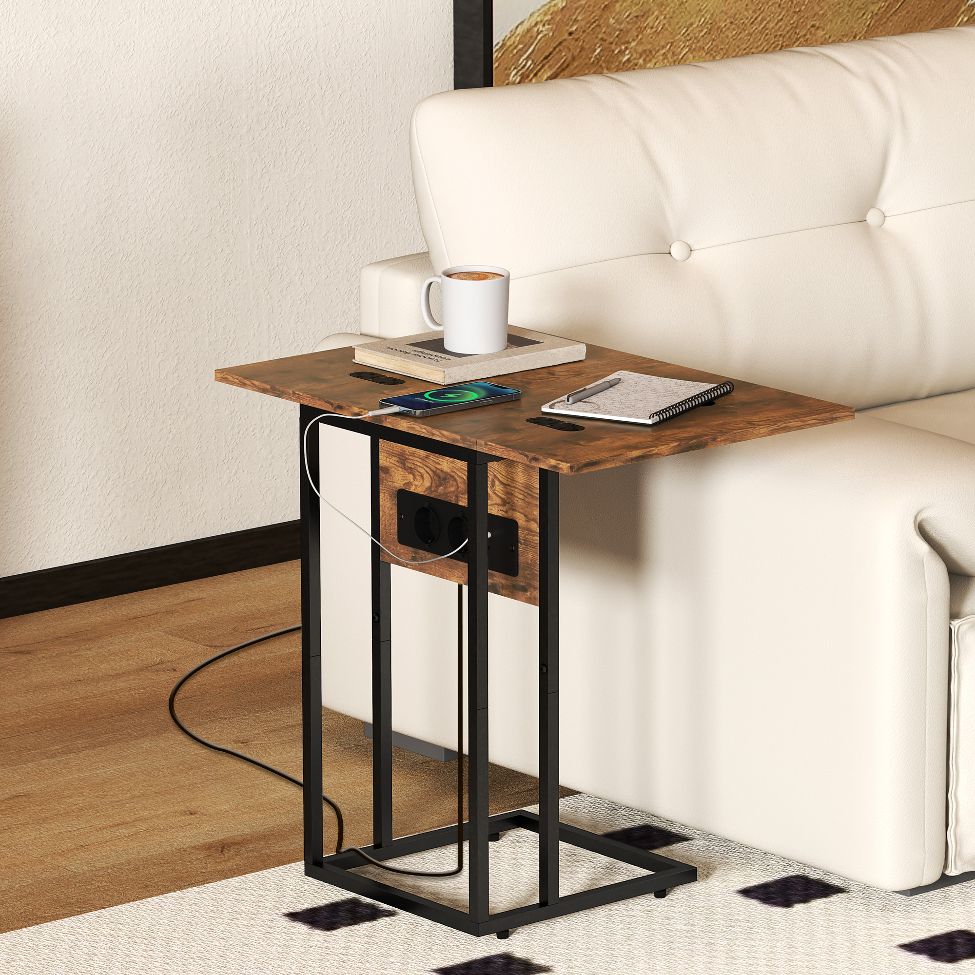 Una mesa auxiliar con un teléfono cargando, una taza y un cuaderno junto a un sofá blanco. Marco de metal negro y enchufes.