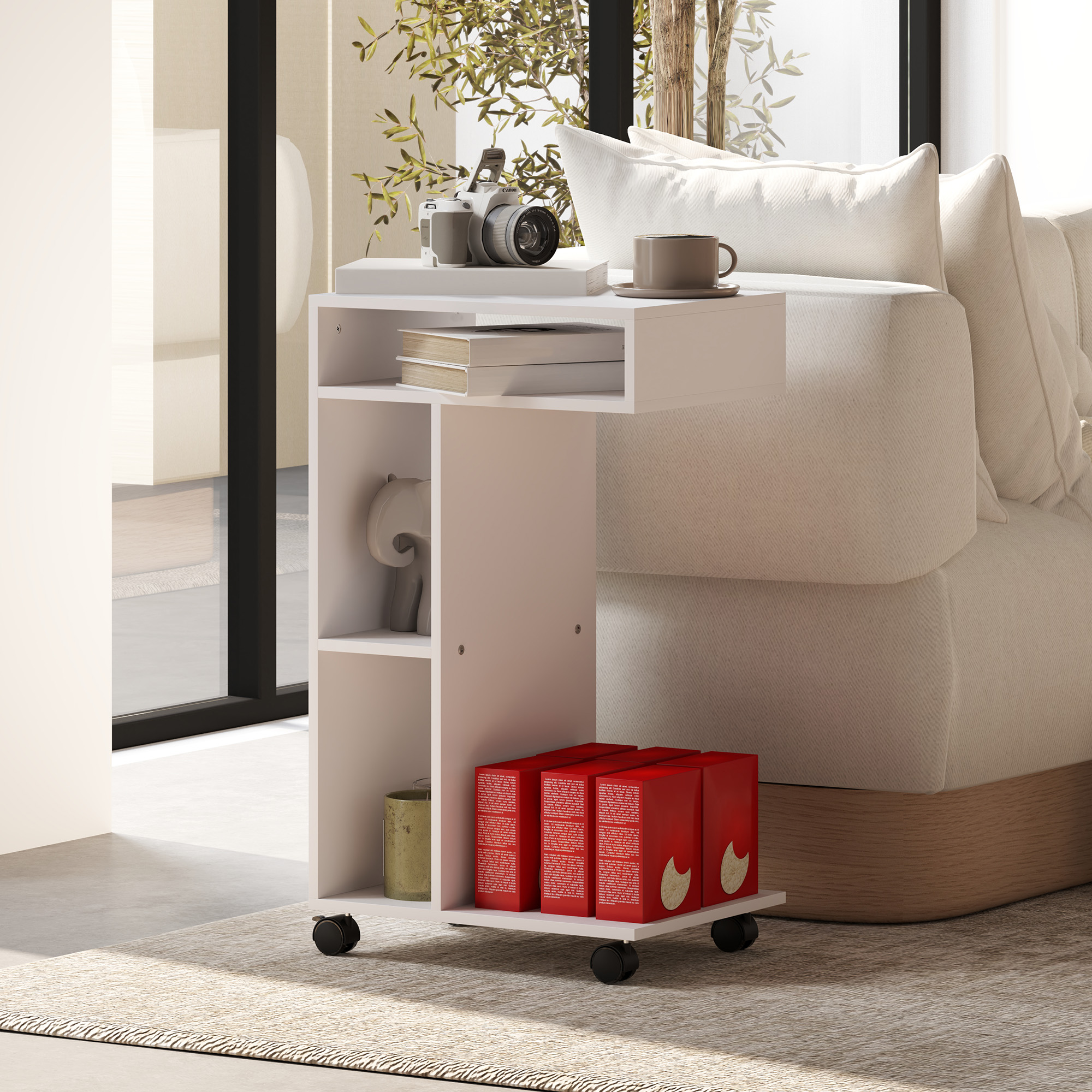 Mesa auxiliar blanca con cámara, libros y taza de café. Cajas rojas en el estante inferior. Una cama al fondo.