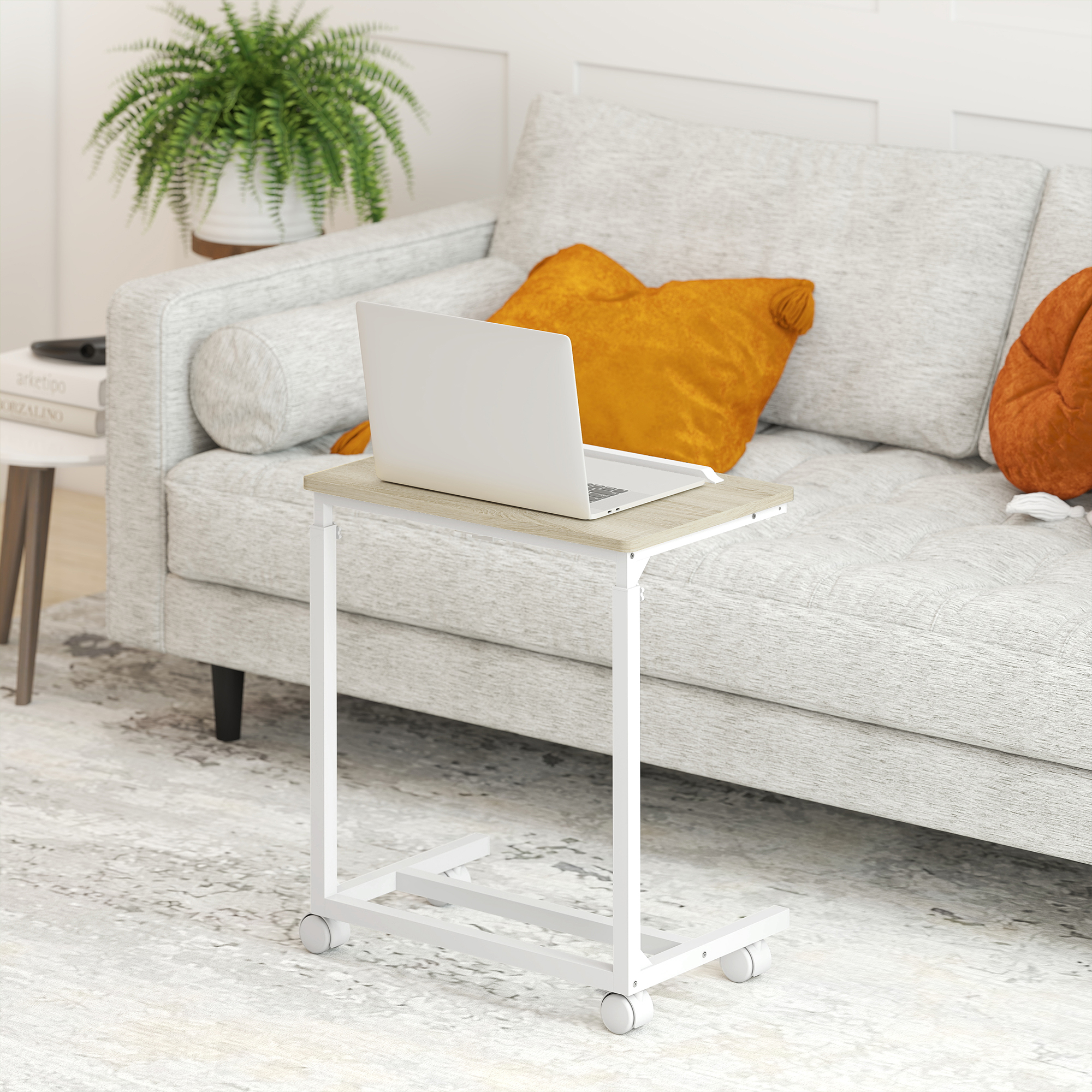 Una laptop sobre una mesa auxiliar con ruedas. Un sofá al fondo, con almohadas naranjas. Una planta en una mesa auxiliar.