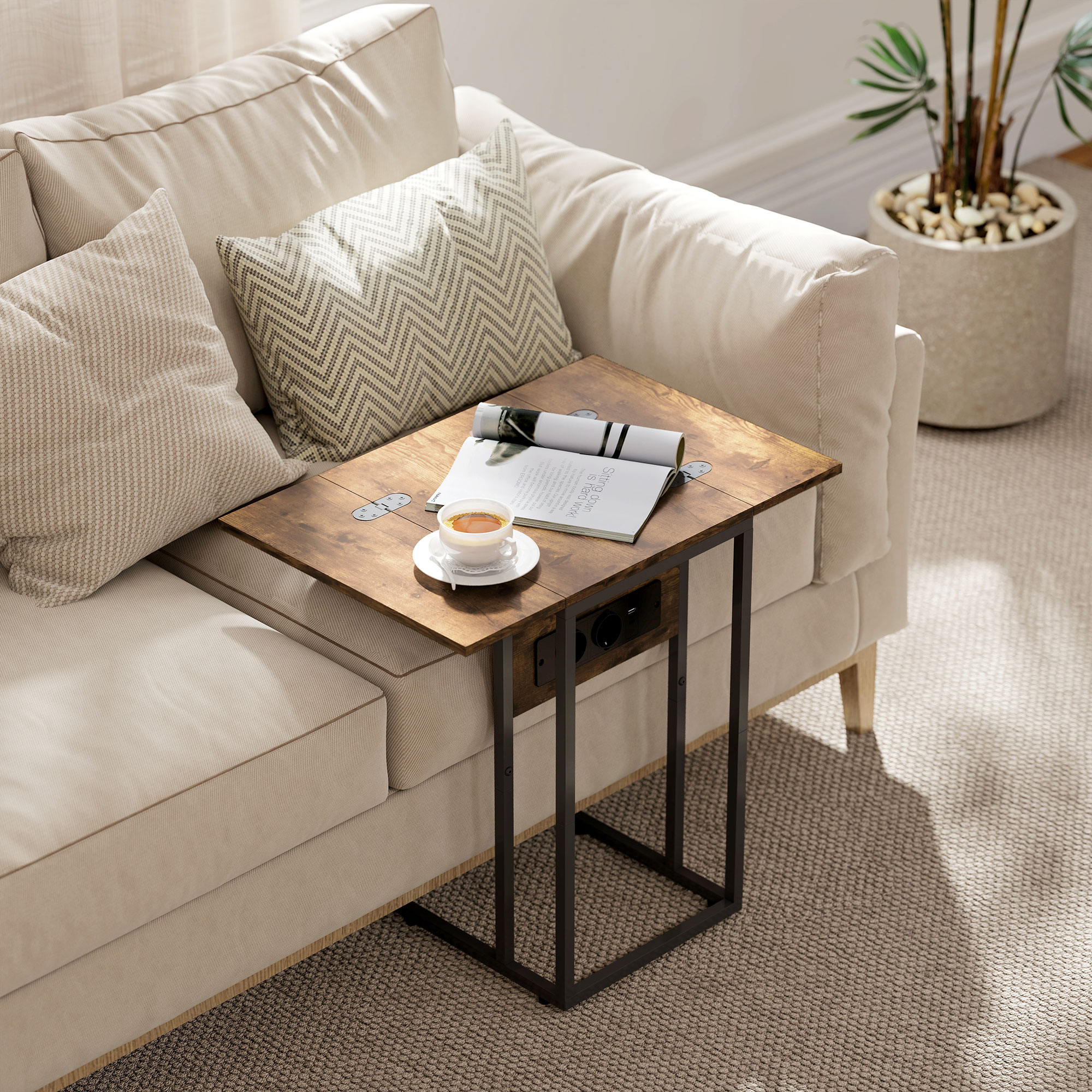 Una mesa auxiliar con café y revista junto a un sofá beige. Una planta está en el fondo.