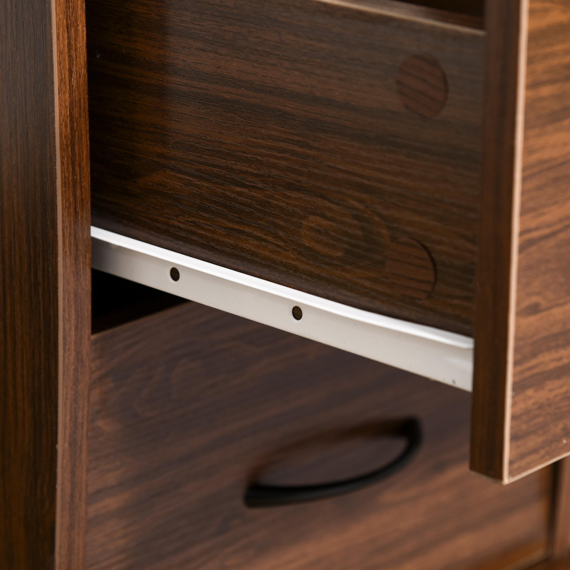 Primer plano de un mueble de madera con un cajón abierto. Guías de cajón de metal blanco y tirador negro. Madera marrón oscura.