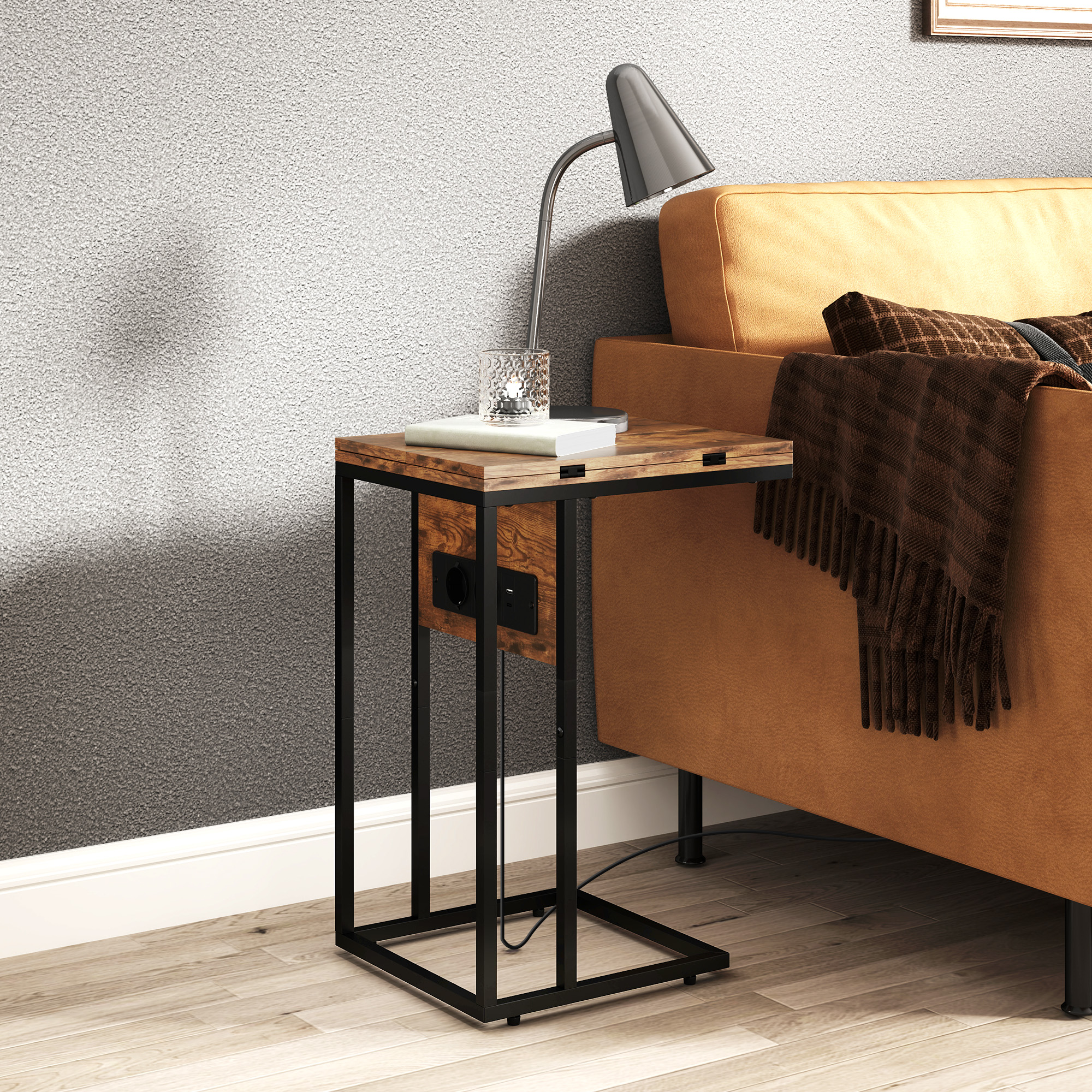 Una mesa auxiliar con lámpara, libro y vaso encima, junto a un sofá marrón. Pared gris al fondo.