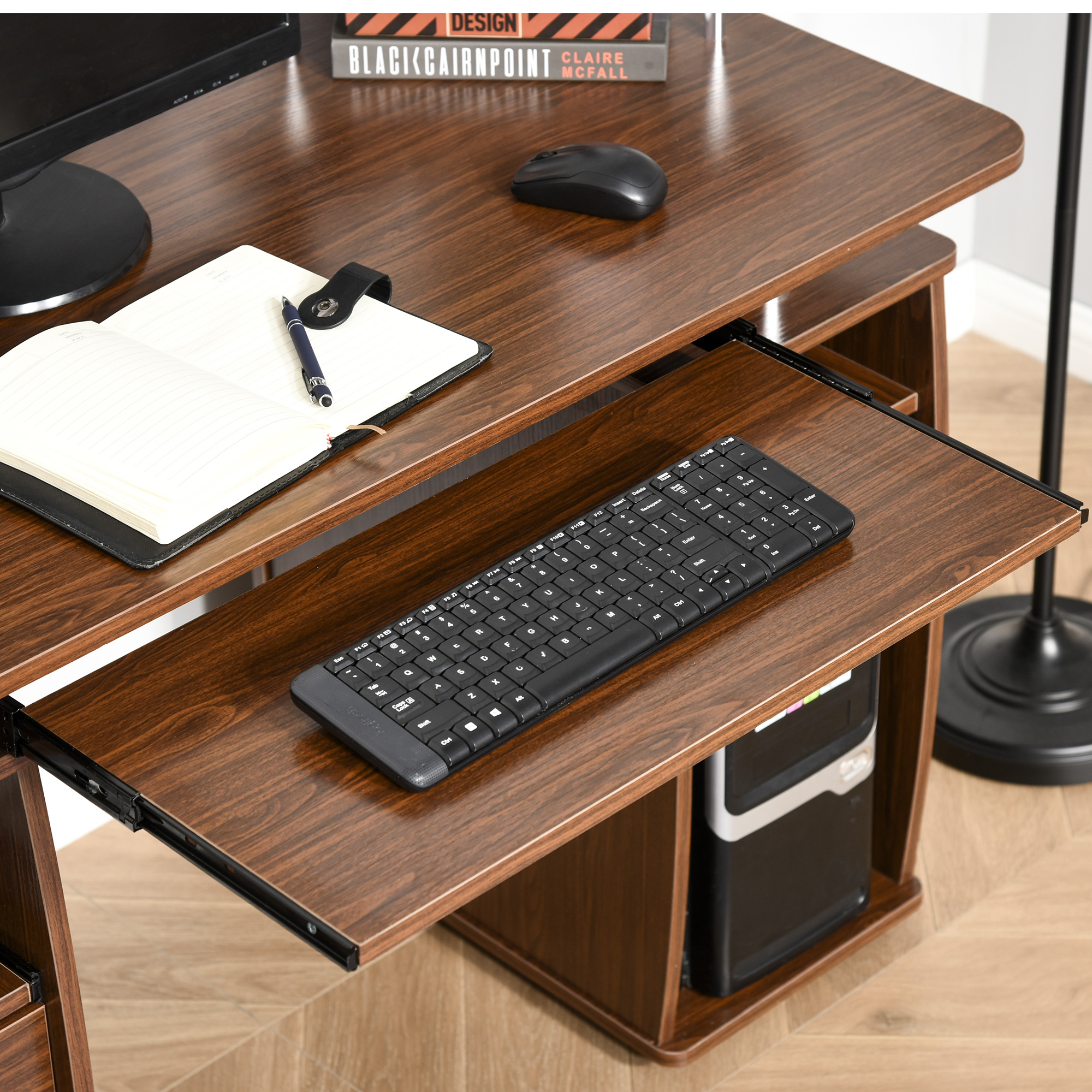 Un escritorio de computadora con teclado, monitor, ratón y cuaderno abierto, todo sobre una superficie de grano de madera marrón.