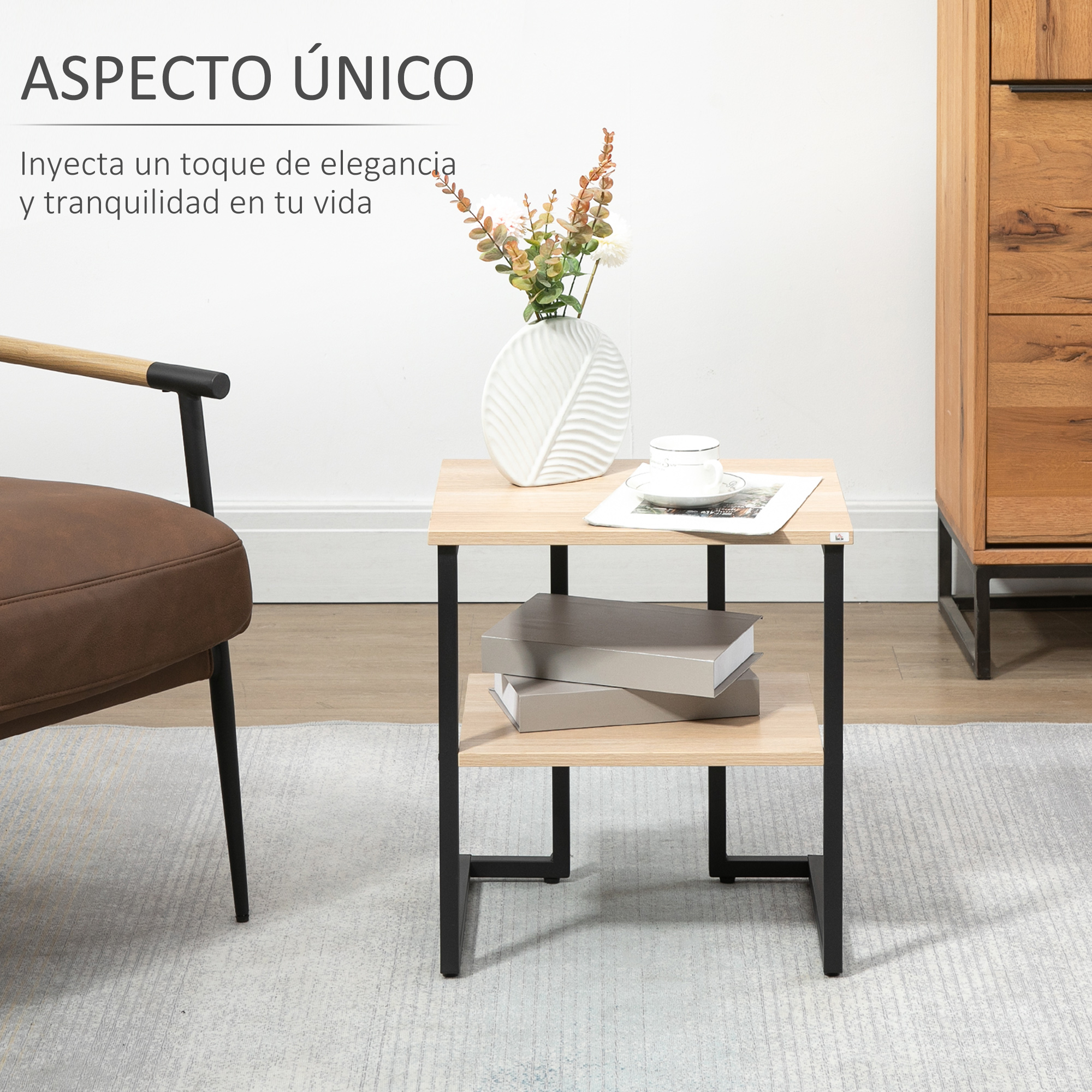 Una mesa de madera pequeña con patas de metal negro. Un jarrón con flores, libros y una taza están sobre la mesa. Una silla a la izquierda.