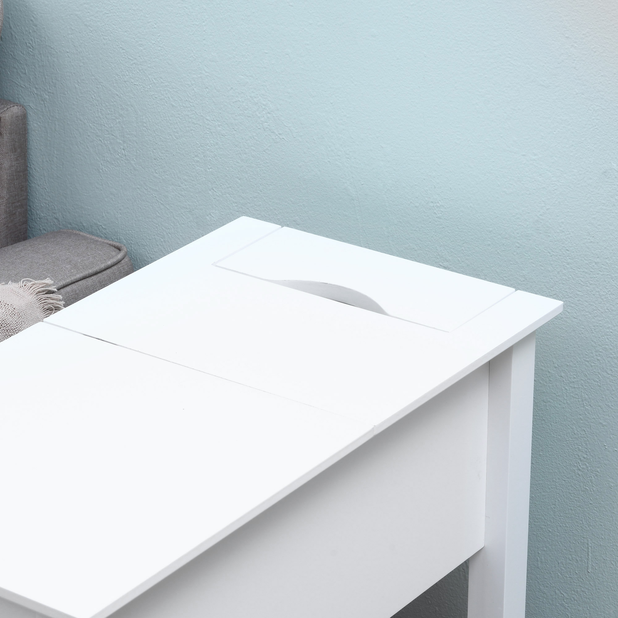 Una mesa blanca con un recorte está frente a una pared azul. Un sofá gris está a la izquierda.