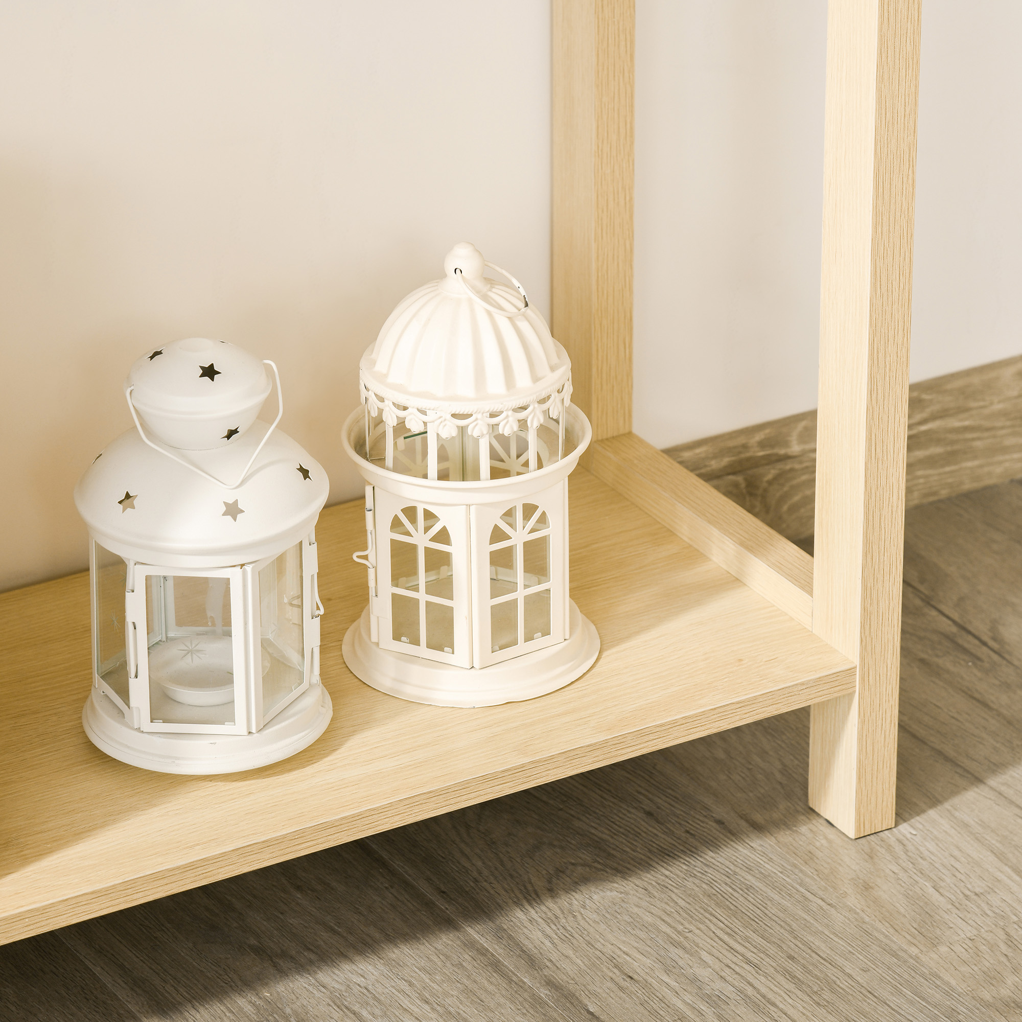 Dos faroles de velas blancos sobre una estantería de madera, con un marco de madera, contra una pared clara y suelo de madera.