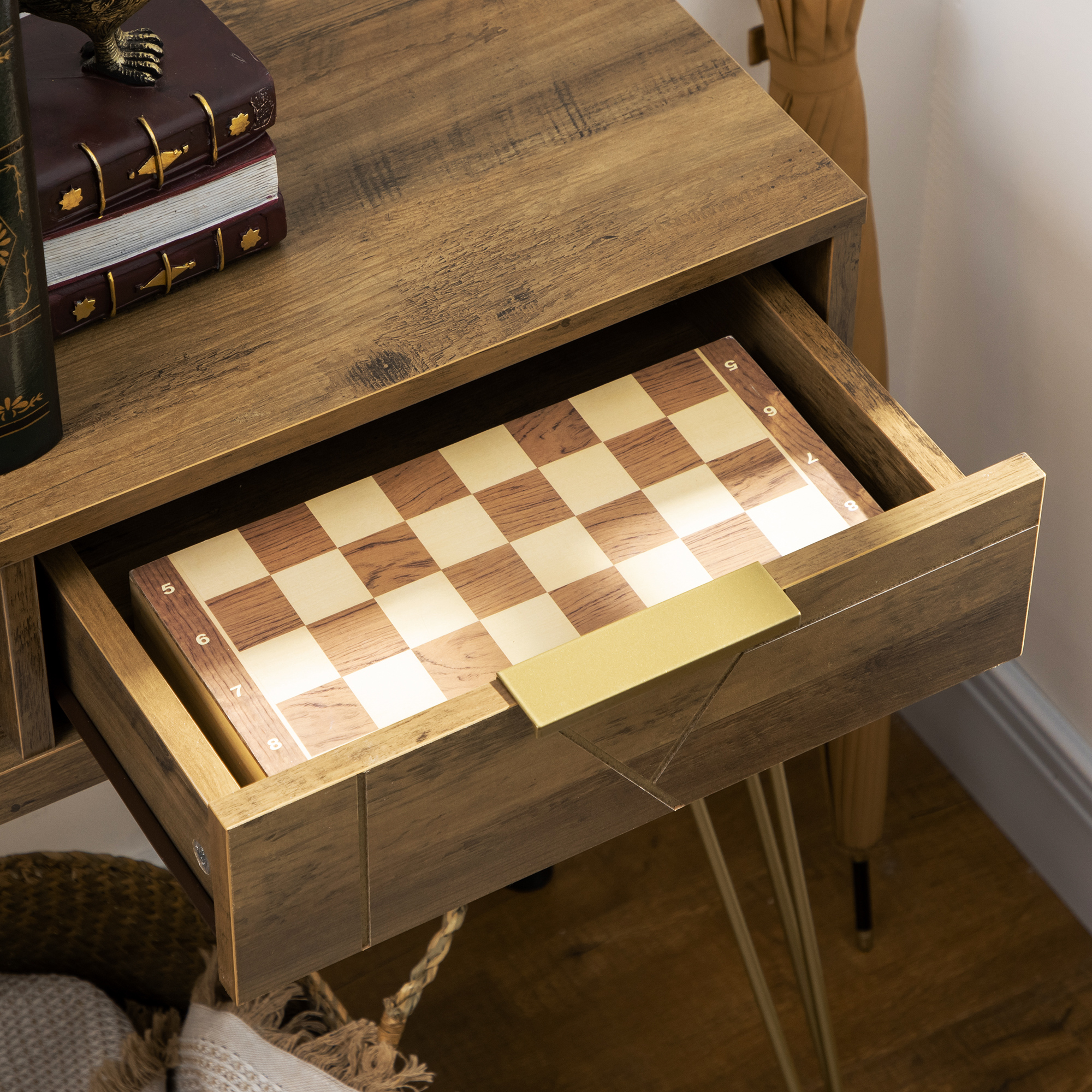 Una mesa de madera con un tablero de ajedrez en el cajón. Libros y una estatua sobre la mesa.