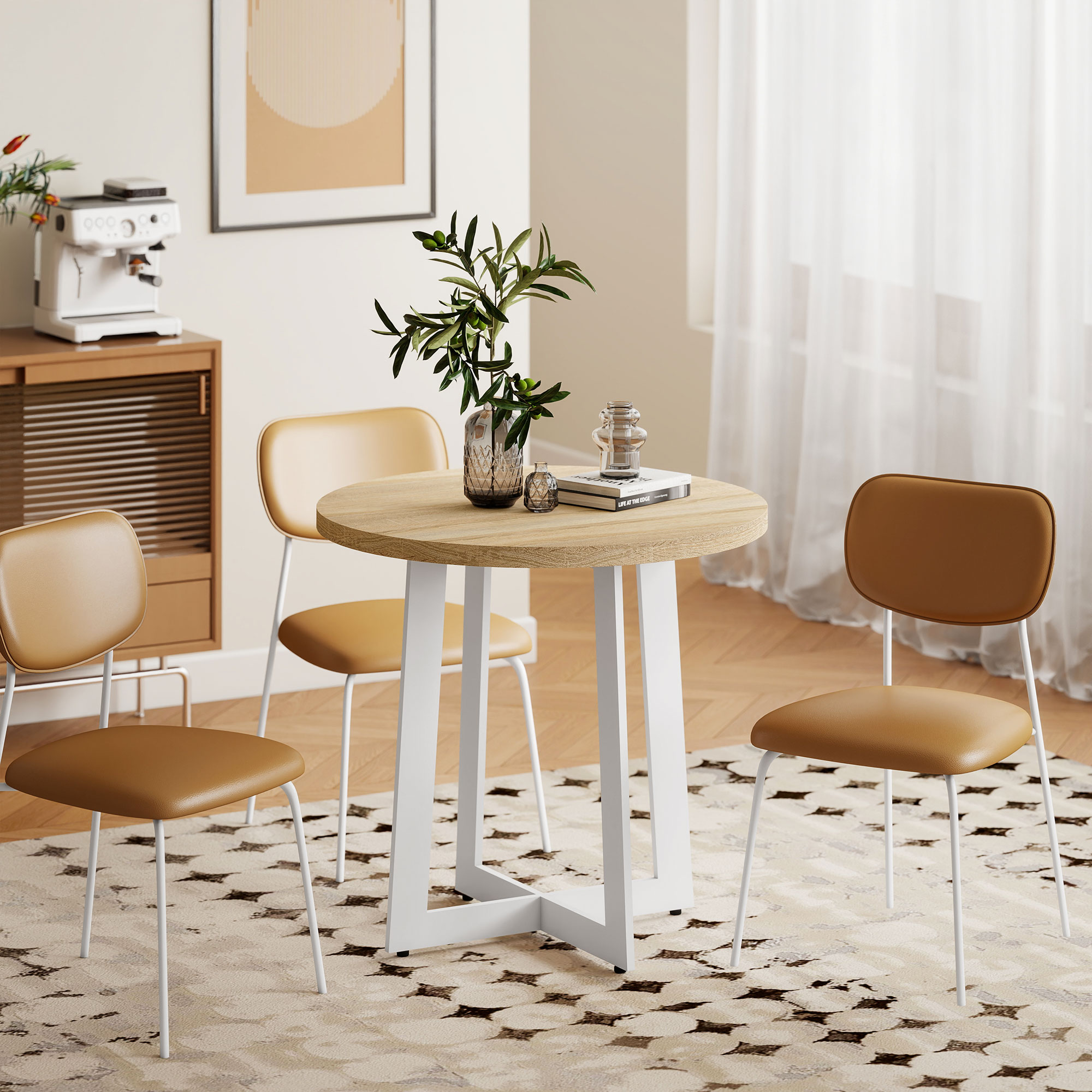 Una mesa redonda de madera con patas blancas está rodeada de cuatro sillas. Una cafetera y un marco de fotos están en la pared.