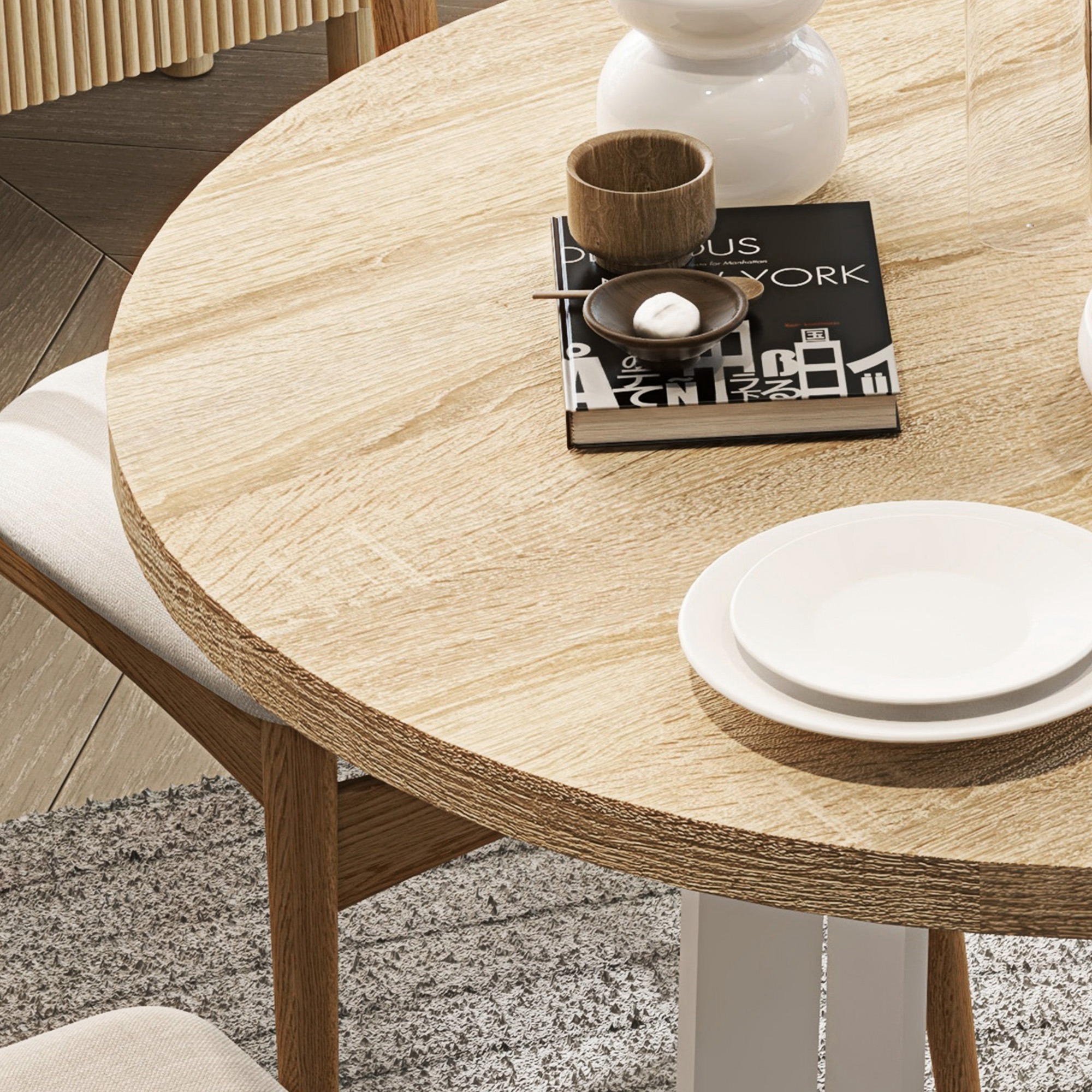 Una mesa redonda de madera con un libro, cuencos pequeños y un jarrón blanco. Dos platos blancos están sobre la mesa.