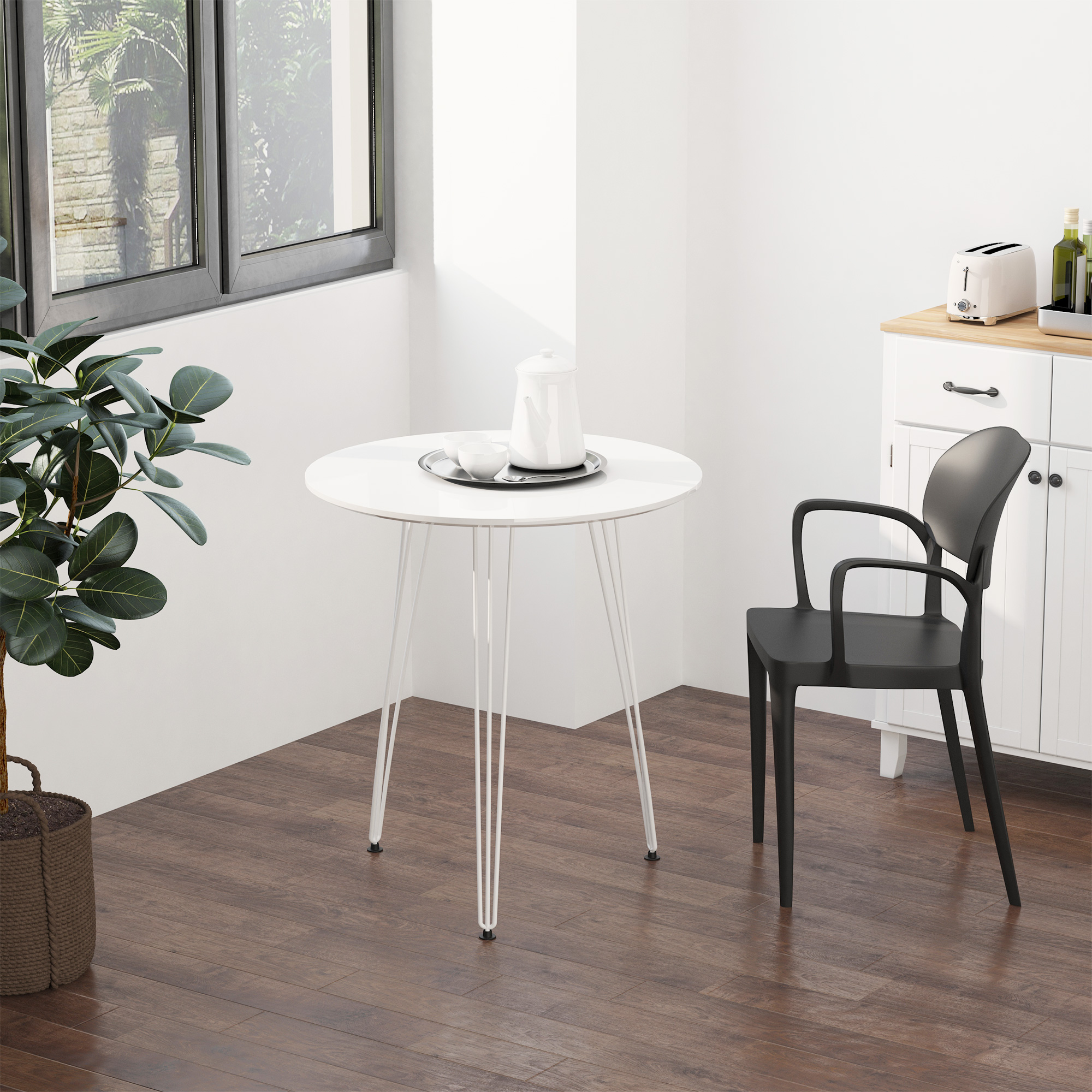 Una mesa blanca con tetera y tazas, una silla negra y una planta en una cesta en una habitación con piso de madera.