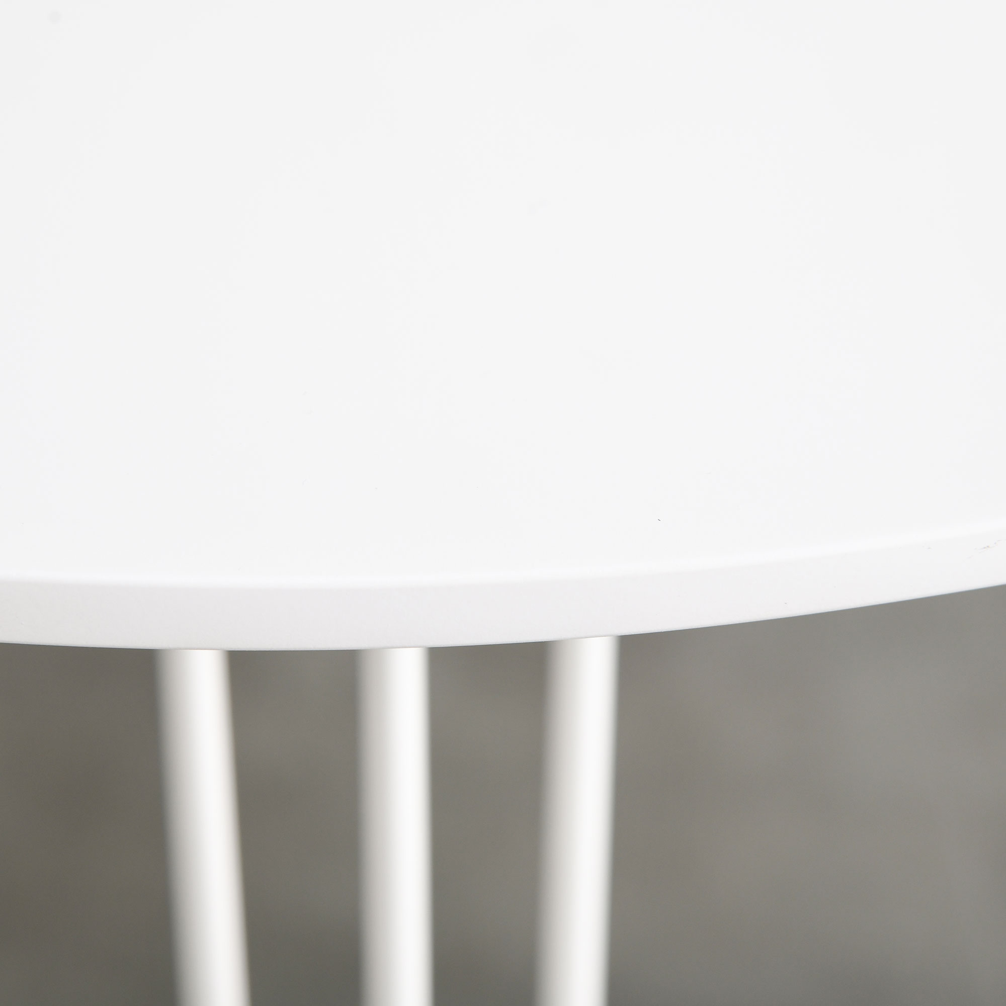 Primer plano de una mesa blanca con tres patas verticales. El fondo es una pared gris lisa.
