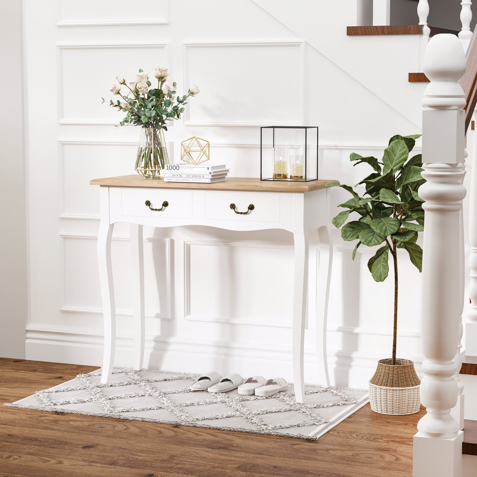Una mesa de entrada blanca con flores, libros y velas, junto a una planta y escaleras. Zapatillas en la alfombra.
