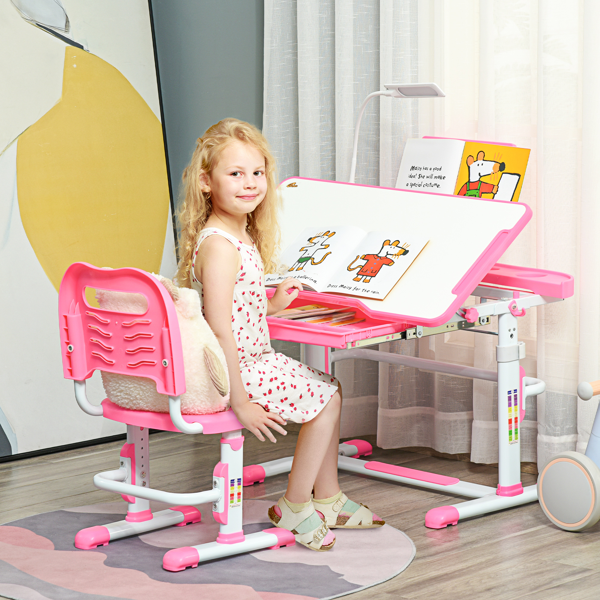 Una niña está sentada en un escritorio rosa, leyendo un libro. Lleva un vestido y sandalias. Hay una lámpara en el escritorio.