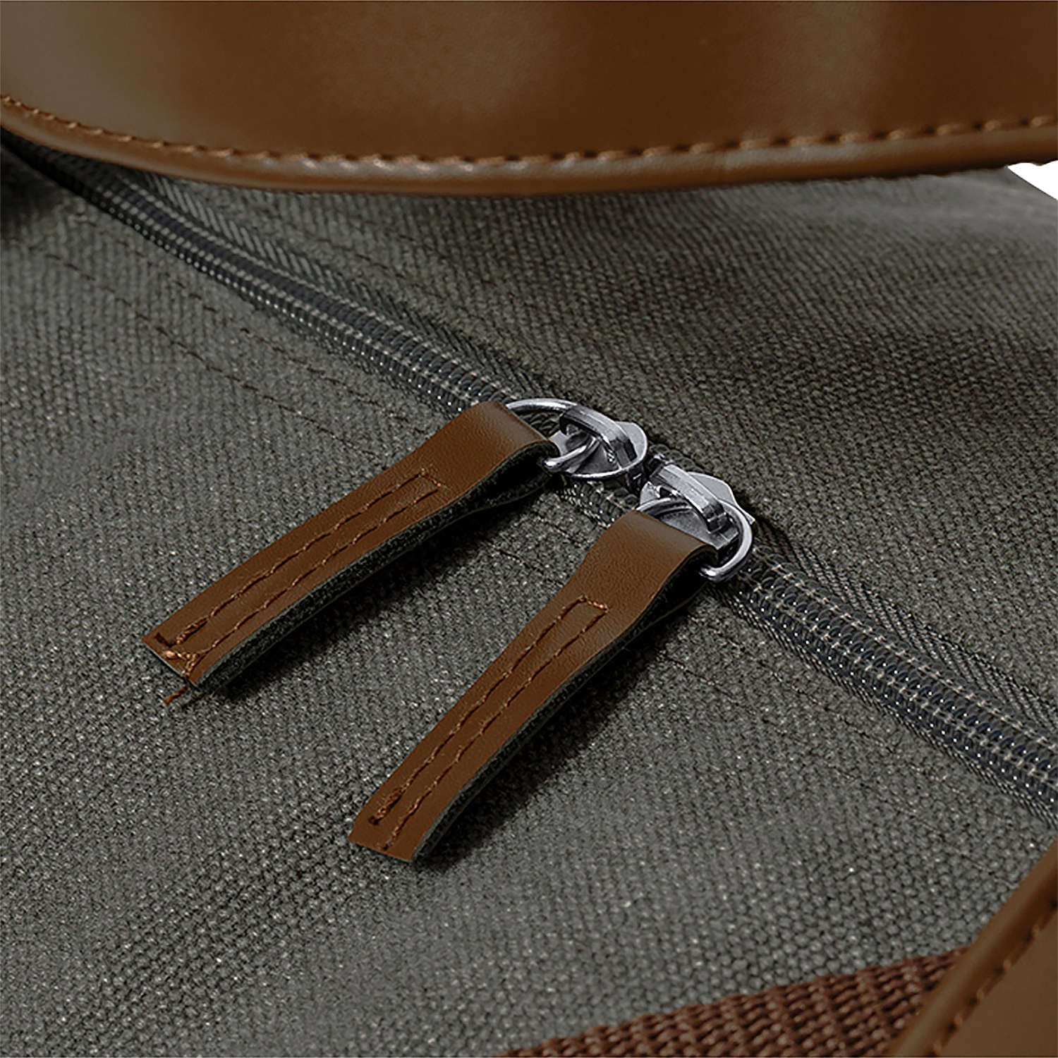 Primer plano de una bolsa de lona con cremallera. Acentos de cuero marrón en los tiradores de la cremallera y borde superior. La lona es gris.
