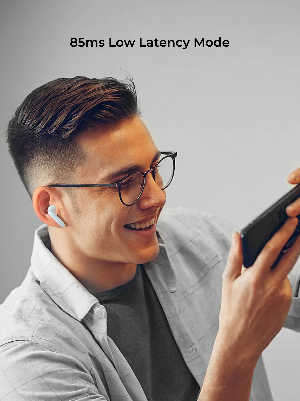 Un hombre con gafas y auriculares sonríe mientras sostiene un teléfono. El texto superior dice: 85ms Low Latency Mode.