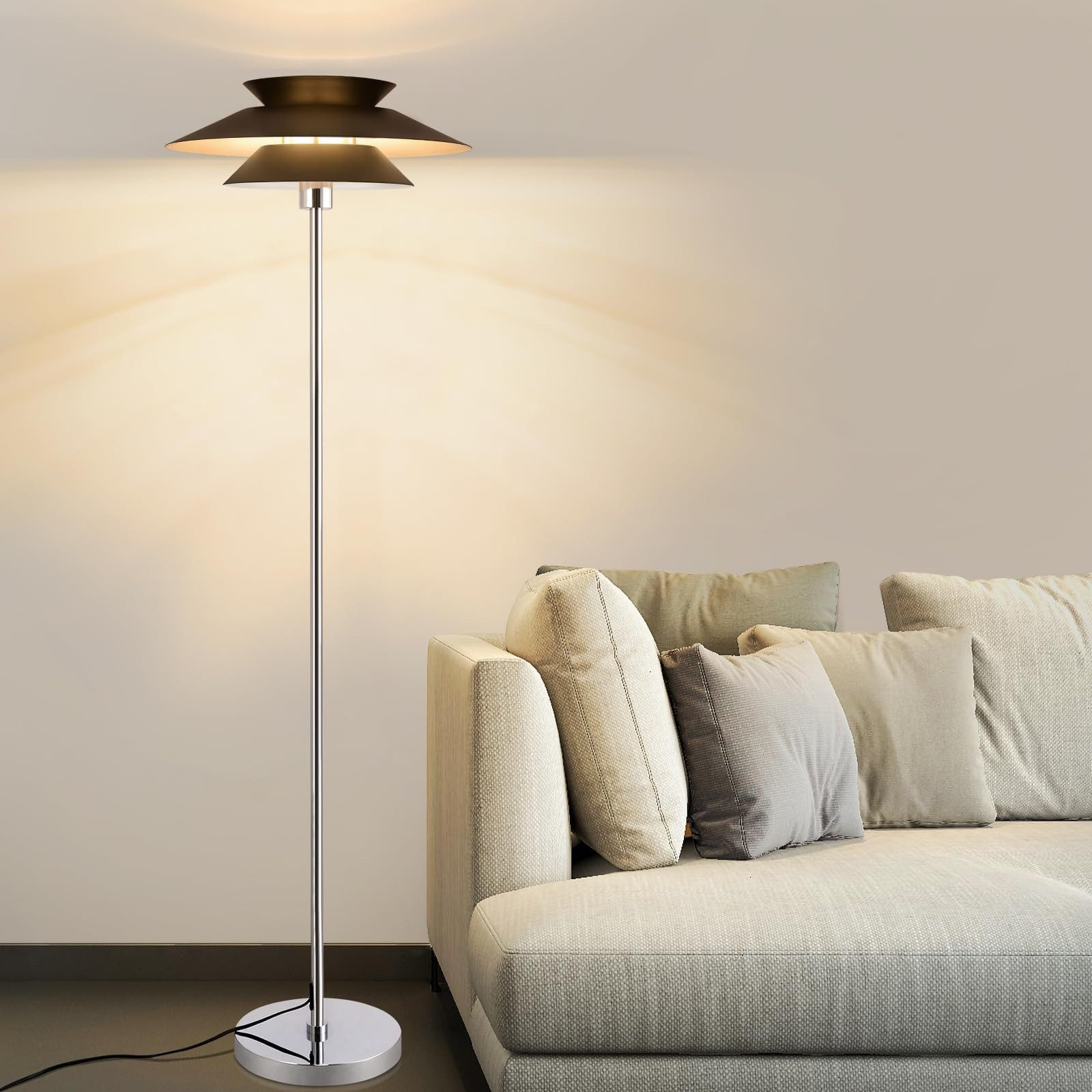 Nowoczesna lampa podłogowa obok sofy z poduszkami. Lampa jest włączona. Ściana i sofa są jasne.