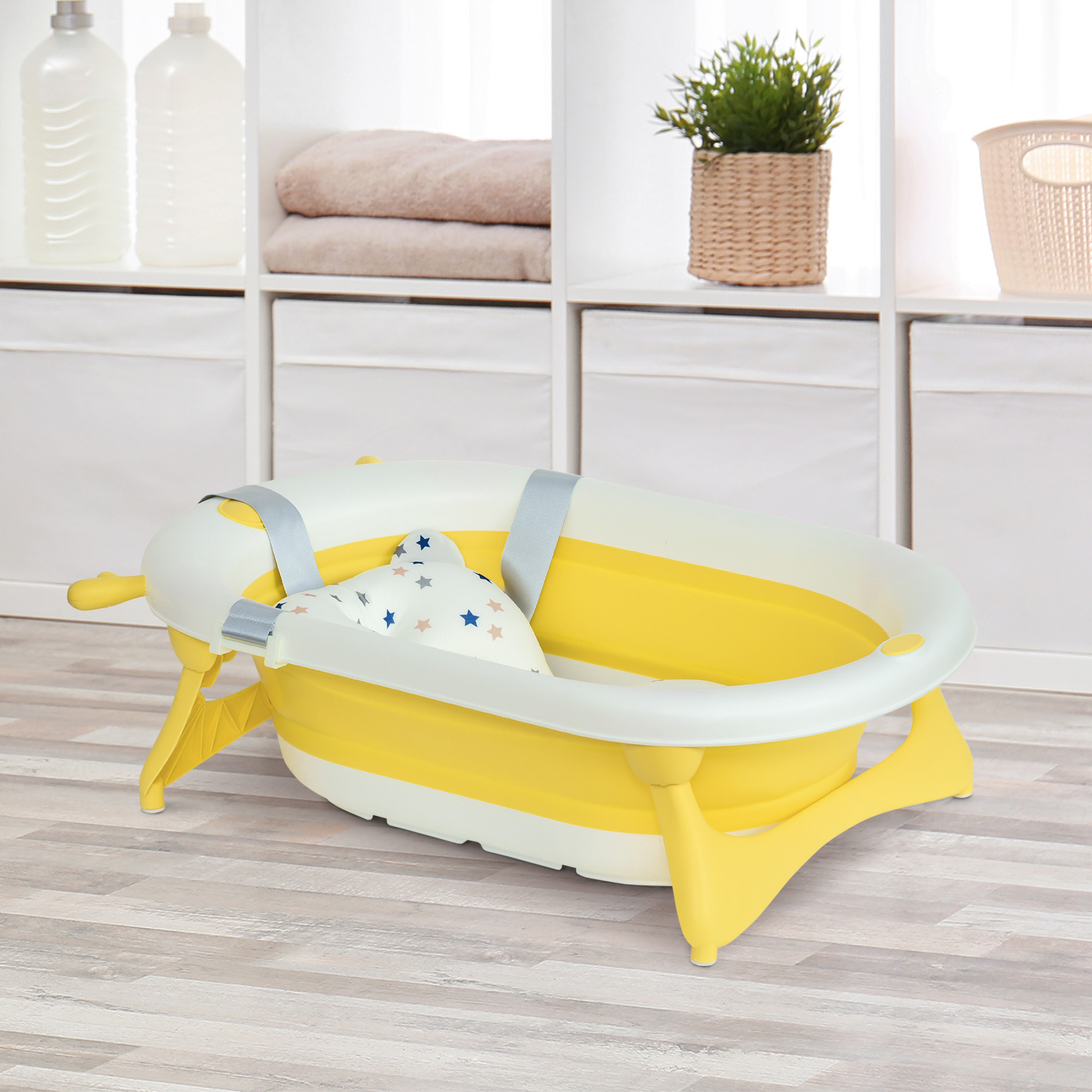 Bañera para bebés amarilla y blanca con almohada con estampado de estrellas. Estantes al fondo con toallas y artículos de aseo.
