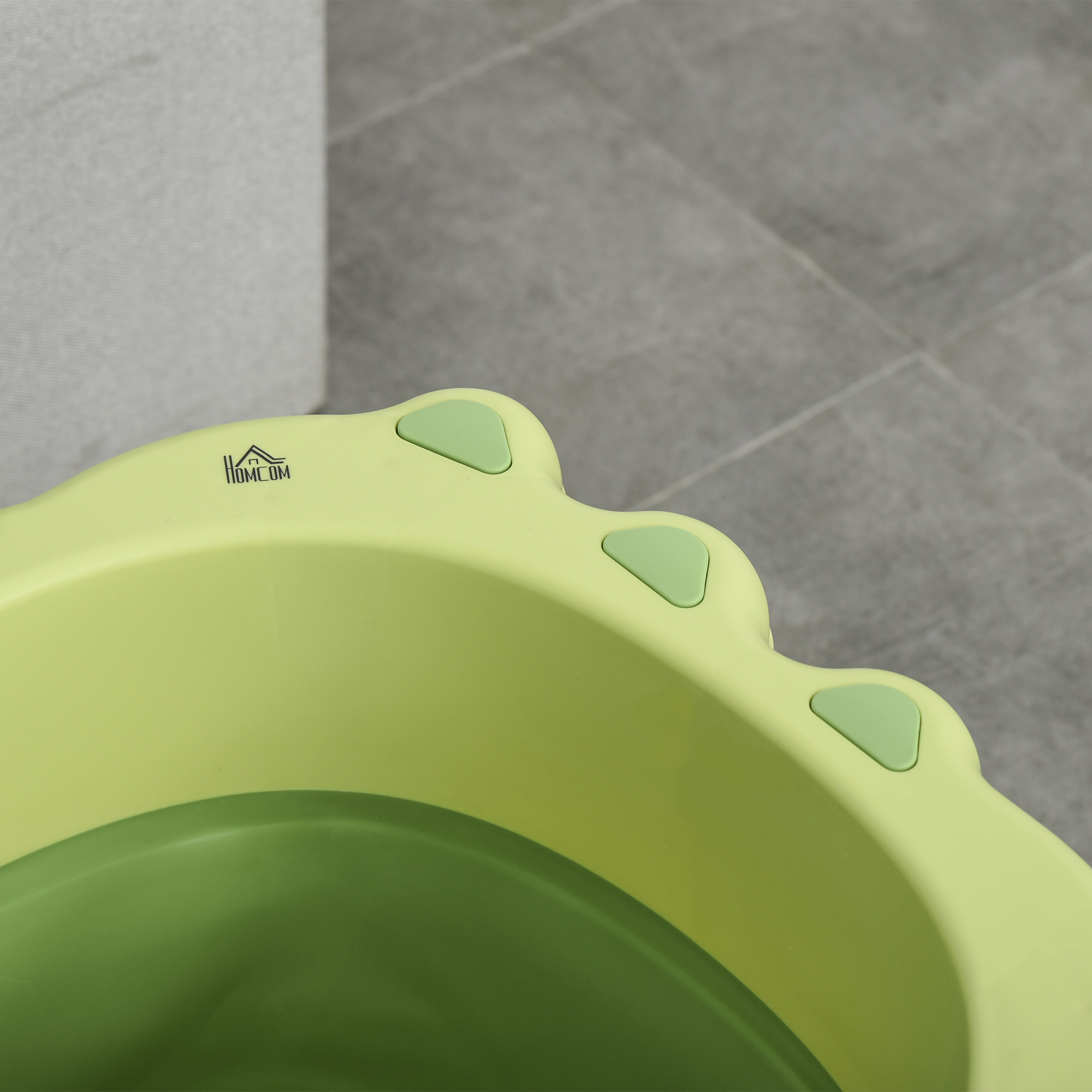 Vista de cerca de una bañera para bebés verde y verde claro, con suelo de baldosas al fondo.