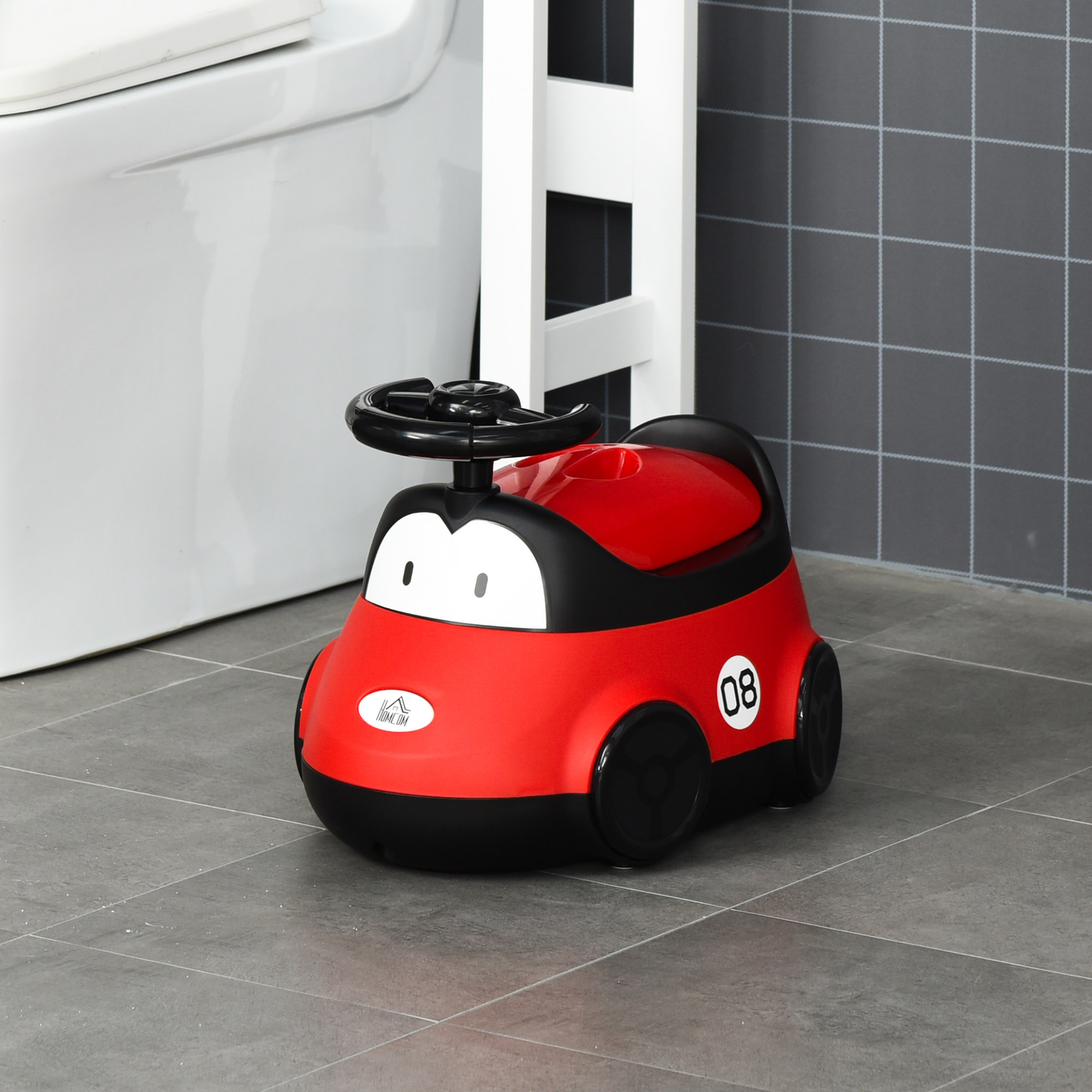 Asiento de entrenamiento para ir al baño con forma de coche rojo y negro sobre suelo embaldosado junto a inodoro y divisor blanco.