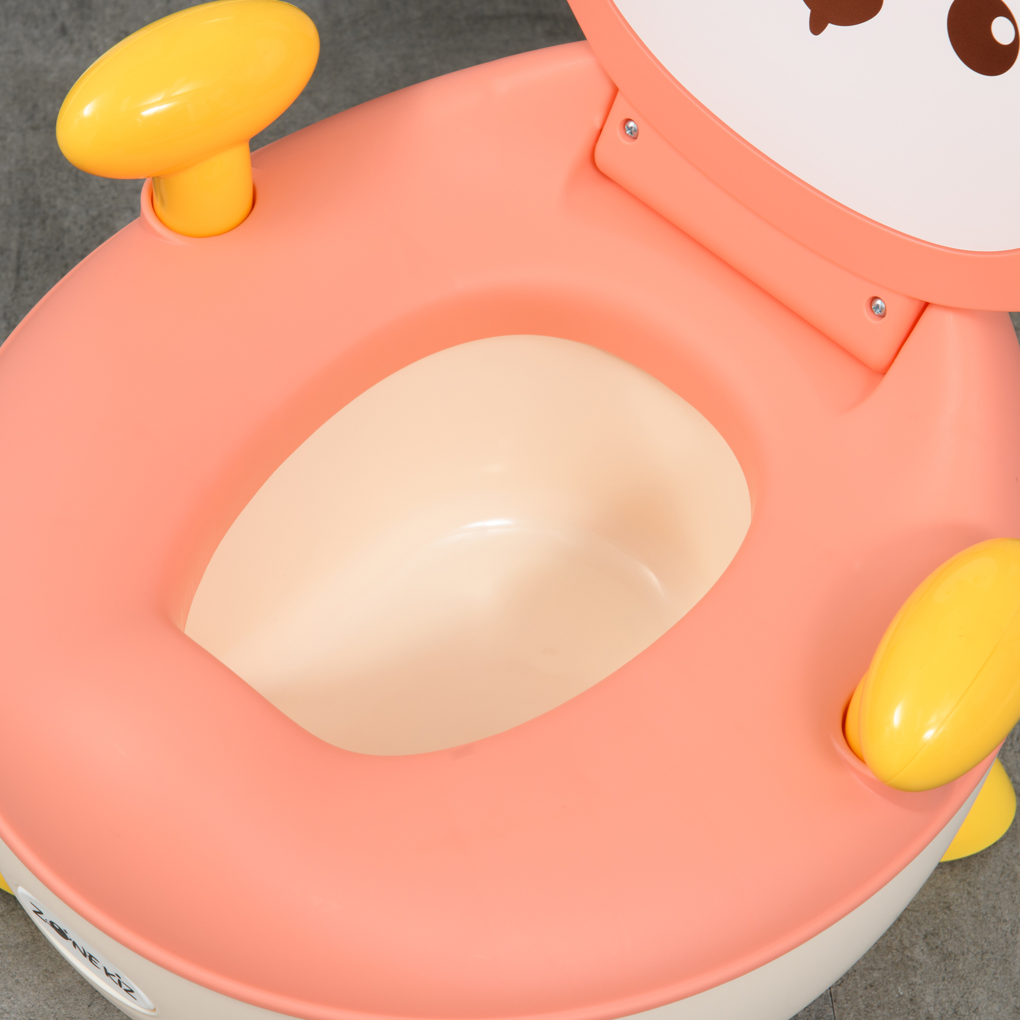 Un asiento de inodoro para bebés rosa y beige con asas amarillas. El asiento tiene una cara de dibujos animados en la parte posterior. Fondo gris.