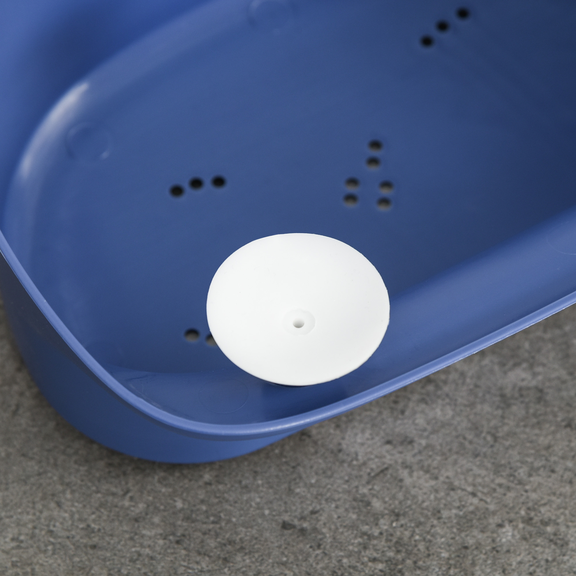 Una bola blanca está en un recipiente de plástico azul. El fondo es una superficie de hormigón gris.