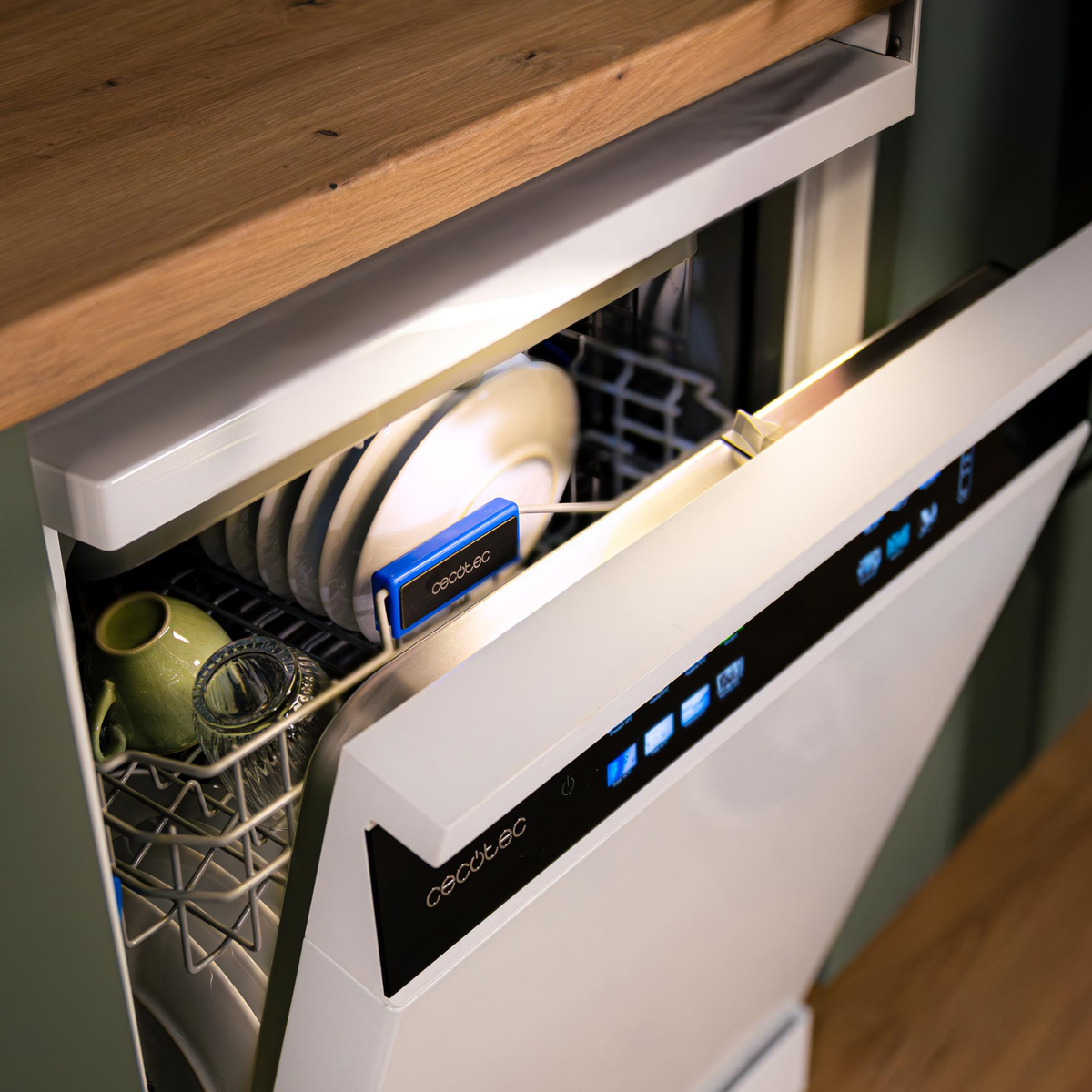 Zmywarka z otwartymi białymi drzwiami. W środku talerze, szklanki i kubek. Widoczne jest niebieskie urządzenie z nazwą marki.