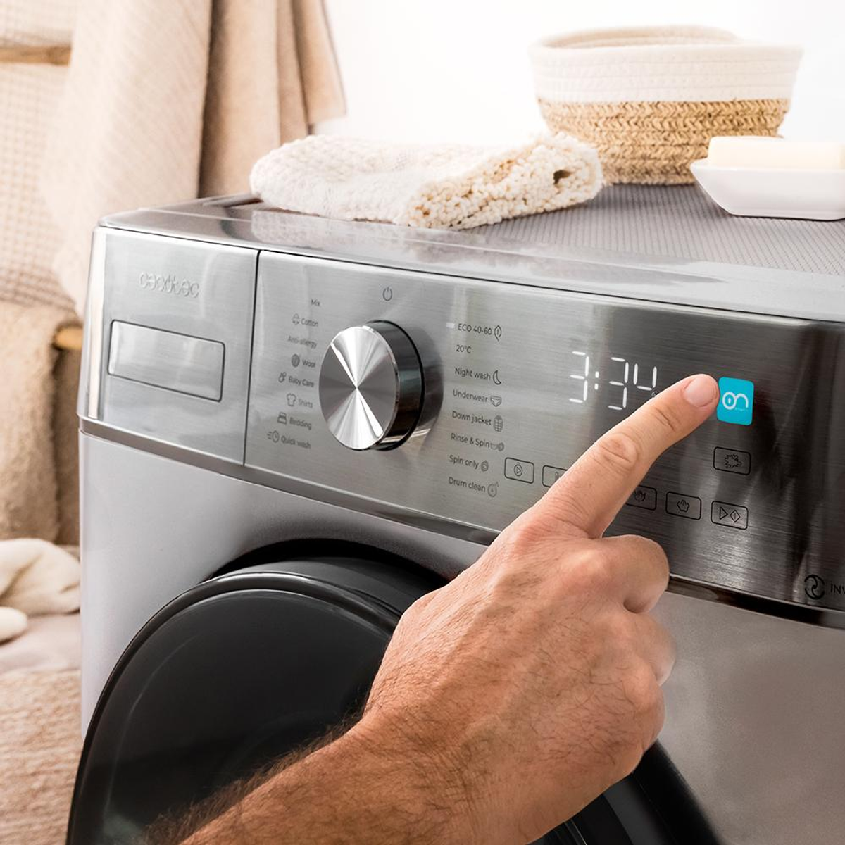 Ręka naciska przycisk na pralce. Wyświetlacz pokazuje 3:34. Na górze pralki znajduje się kosz i ręcznik.