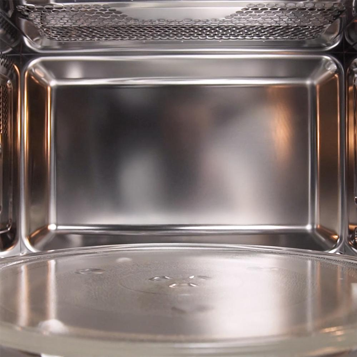 Wnętrze kuchenki mikrofalowej. Szklany talerz na dole, wnętrze ze stali nierdzewnej. Na górze metalowa siatka.