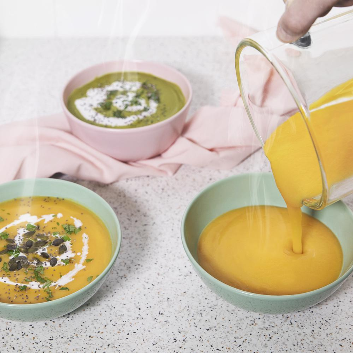 Tres cuencos de sopa. Uno verde, un cuenco rosa con sopa y una mano vertiendo sopa naranja en un cuenco verde.