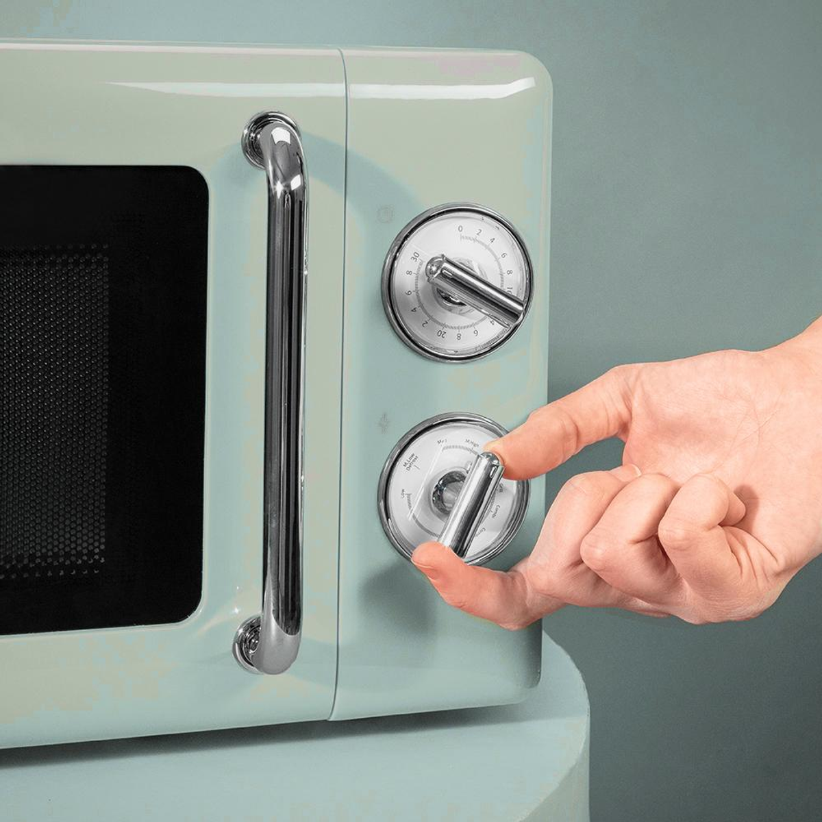 Ręka regulująca pokrętło kuchenki mikrofalowej. Kuchenka mikrofalowa jest miętowo-zielona z chromowanymi akcentami. Tło jest stonowane turkusowe.