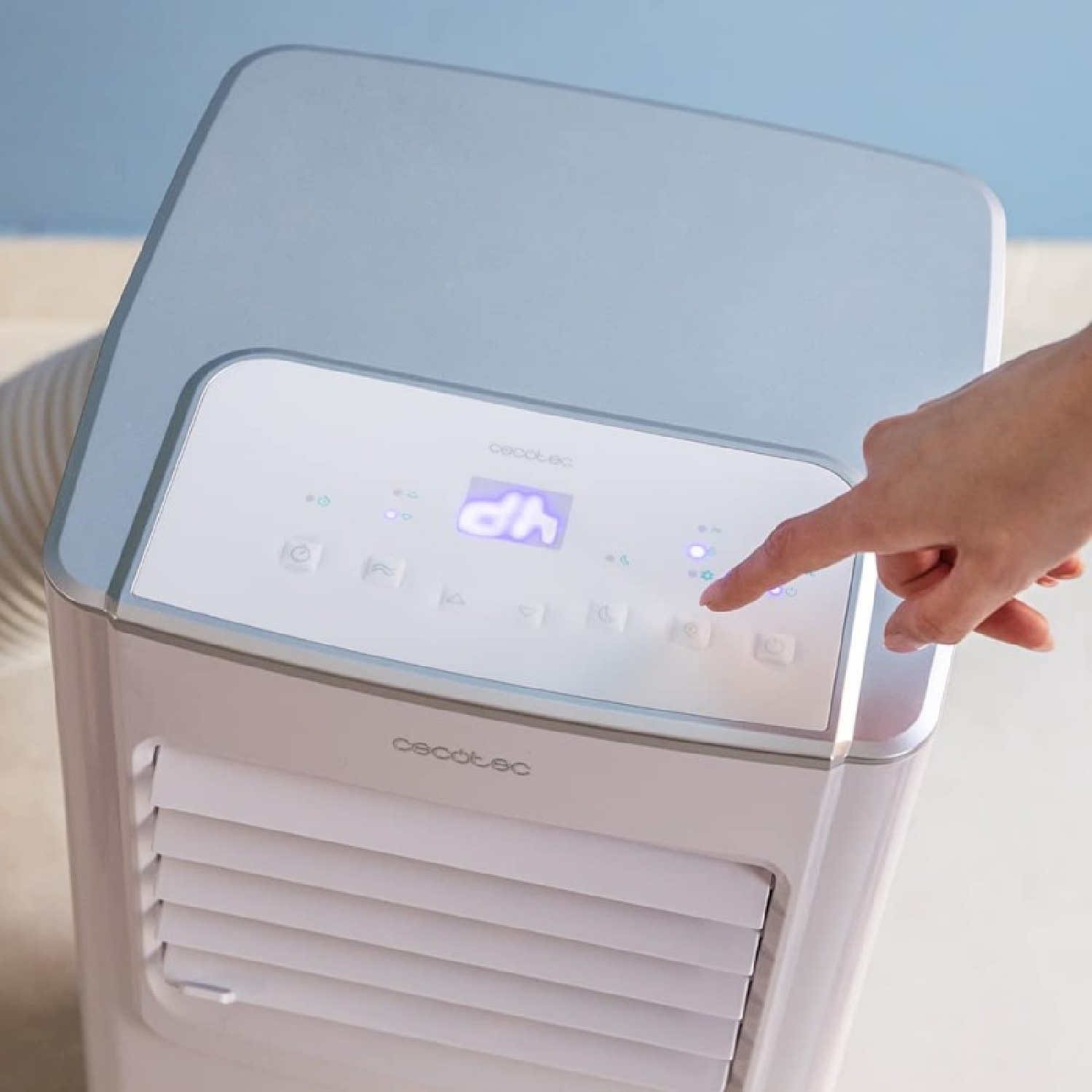 Una mano presiona un botón en un enfriador de aire blanco. El enfriador tiene una pantalla digital y una ventilación. El fondo es azul claro.