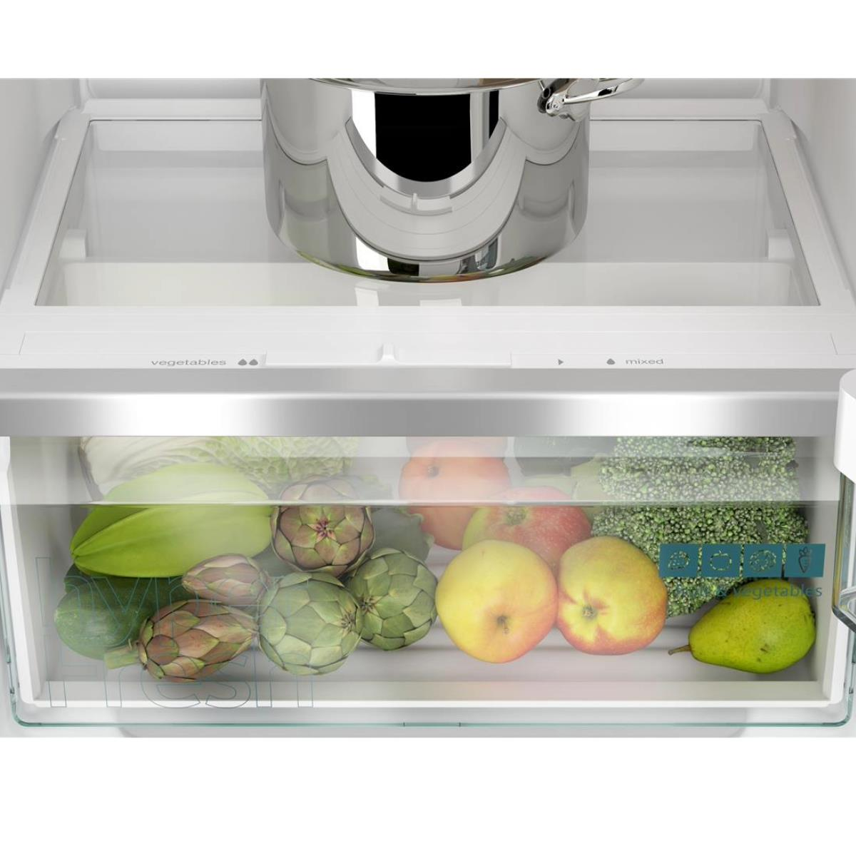 Refrigerator interior. Vegetables and fruits in the drawers, artichokes, apples and pears. A pot on the shelf above.