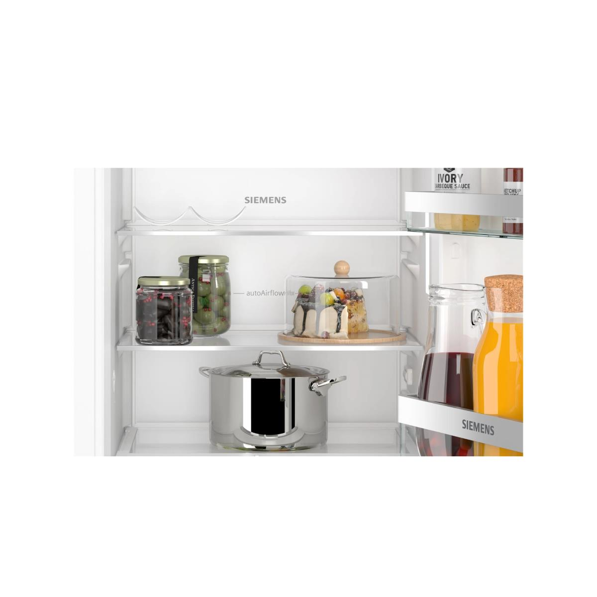 Inside a fridge: jars, cake, pot, and bottles. Jars contain olives and berries. Cake has a glass cover. Bottles hold juice.