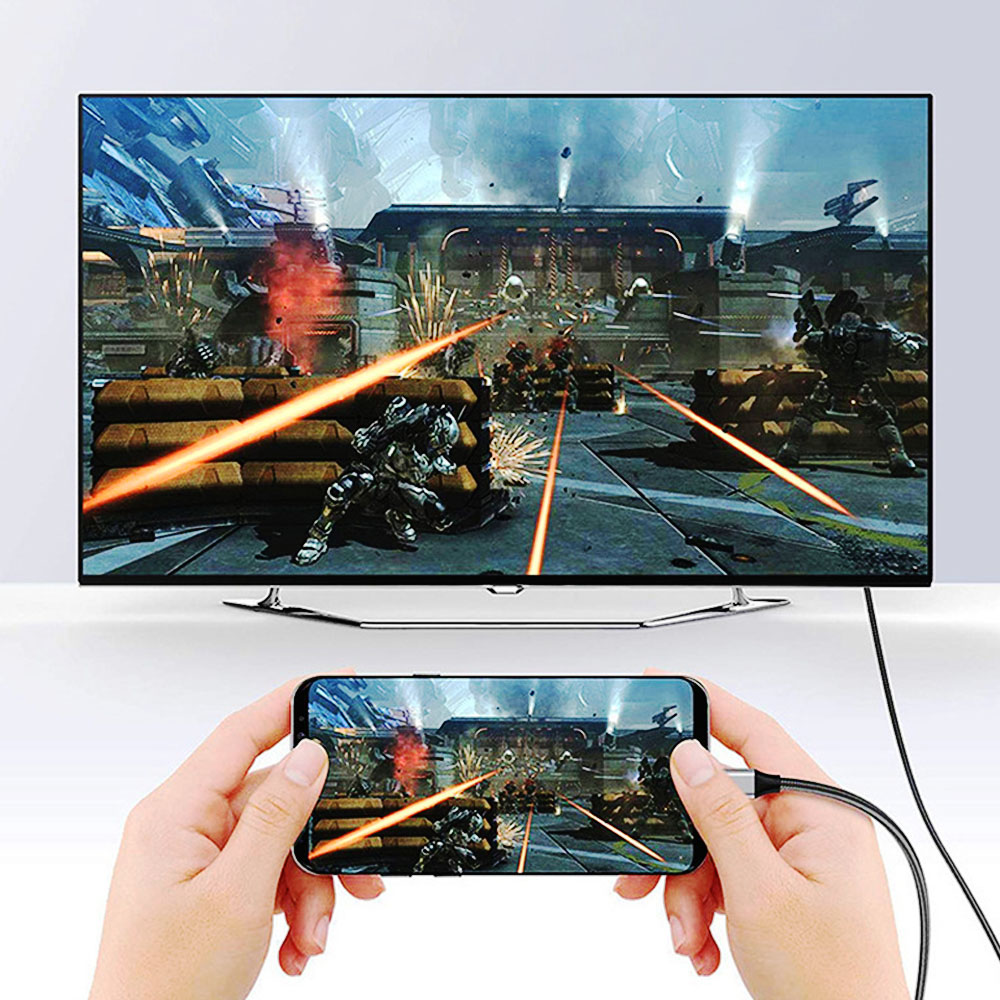 Ręce trzymają telefon, który wyświetla grę wideo na telewizorze. Gra pokazuje żołnierzy, eksplozje i wiązki laserowe.