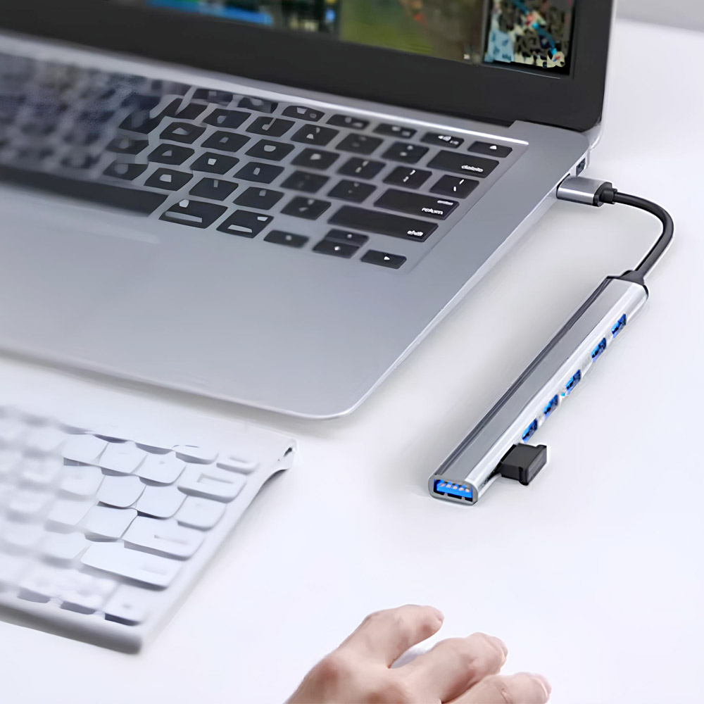 Laptop z podłączonym hubem USB. Biała klawiatura na pierwszym planie. Ręka sięga w stronę huba.
