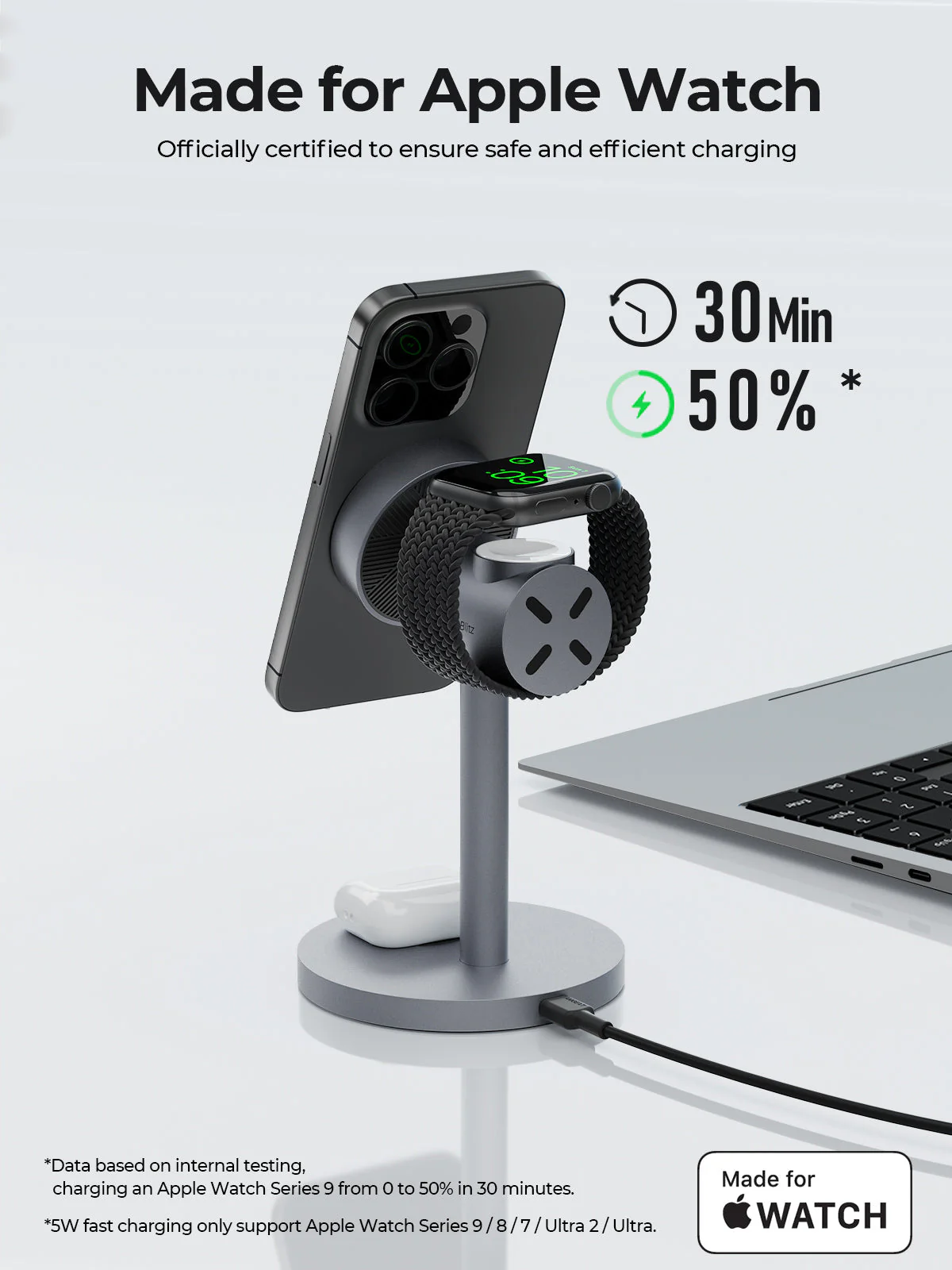 Un soporte de carga gris con un iPhone y un Apple Watch. El reloj muestra el 50% de carga en 30 minutos. Un portátil en el fondo.