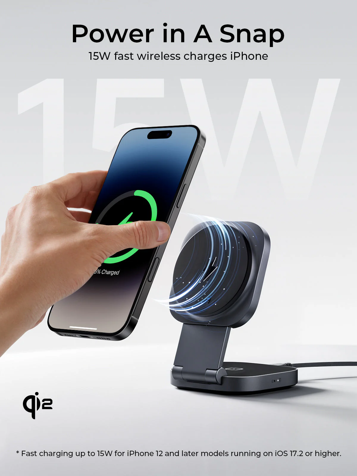 Una mano sostiene un iPhone negro cargando de forma inalámbrica en un soporte de carga negro. El teléfono muestra 5% cargado.
