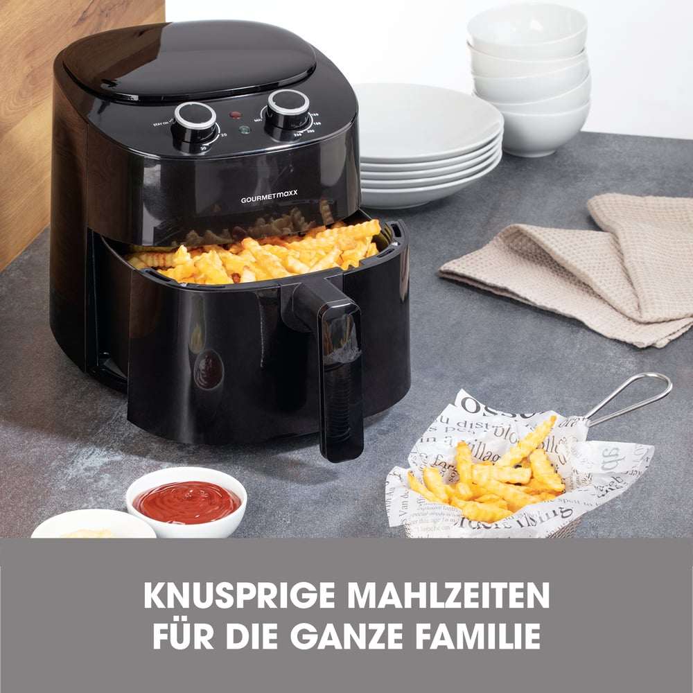 Ein schwarzer Luftfritteuse mit Pommes Frites. Schüsseln, Teller und Saucen stehen auf der Theke. Der Text lautet: KNUSPRIGE MAHLZEITEN FÜR DIE GANZE FAMILIE.