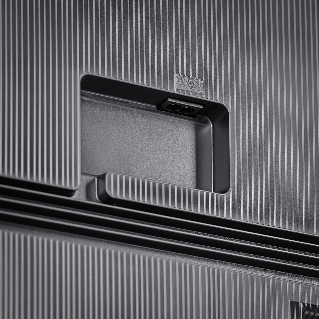 Gros plan d'une surface gris foncé texturée avec des lignes verticales. Une zone encastrée contient un port d'alimentation et un petit symbole.