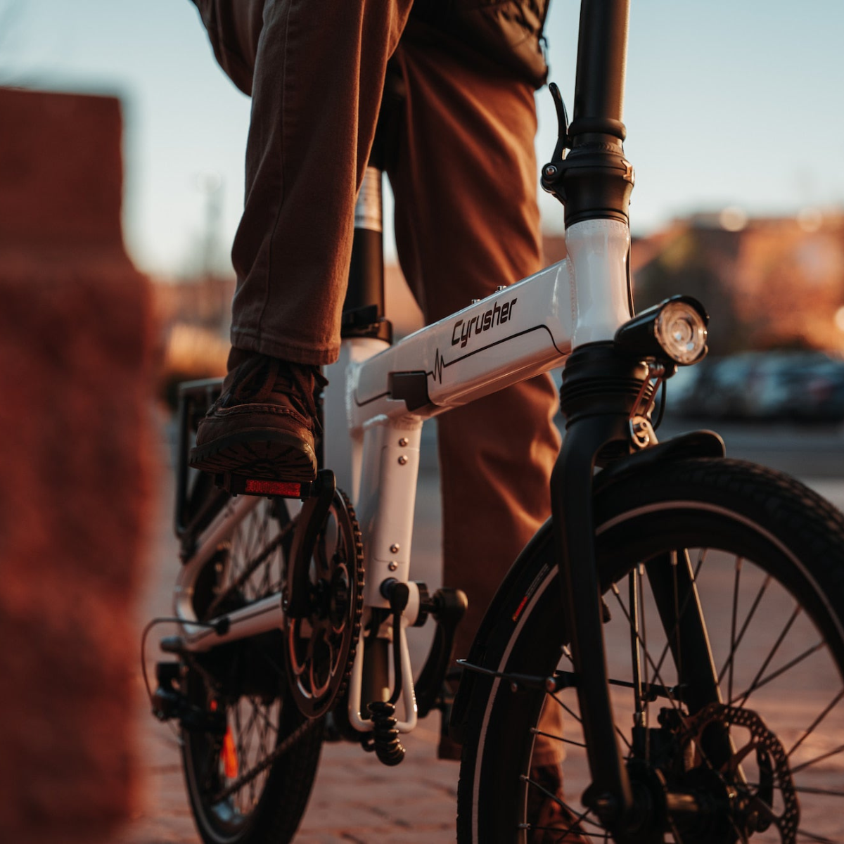 Osoba na białym rowerze Cyrusher. Widoczne jest przednie koło i reflektor roweru. Nogi i stopy osoby są ostre.