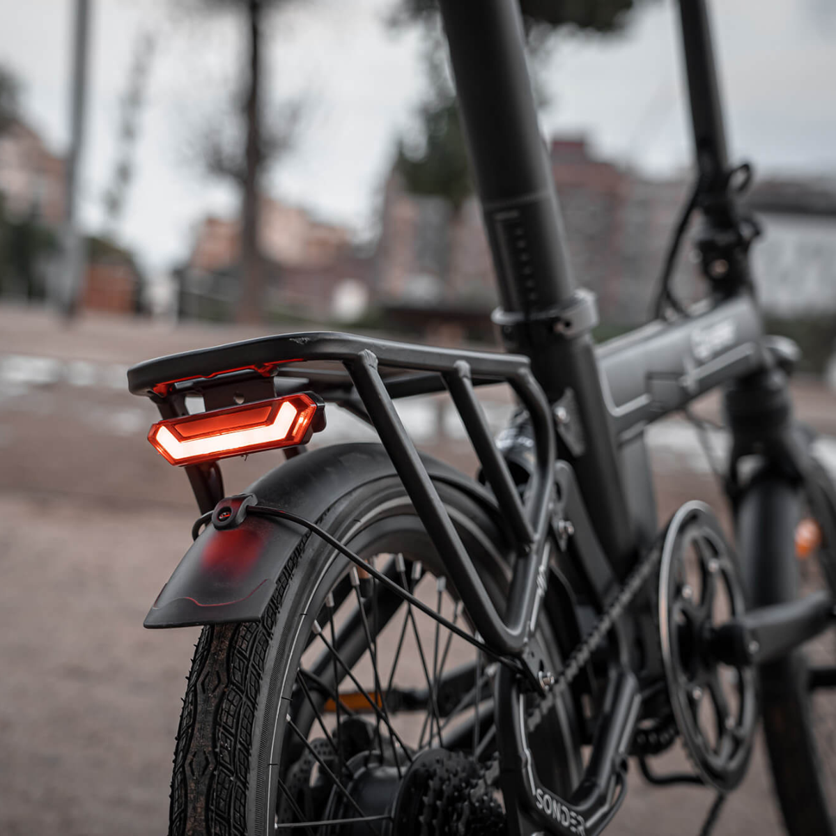 Zbliżenie czarnego roweru elektrycznego. Czerwone tylne światło jest włączone. Bagażnik znajduje się nad kołem. Tło jest rozmyte.