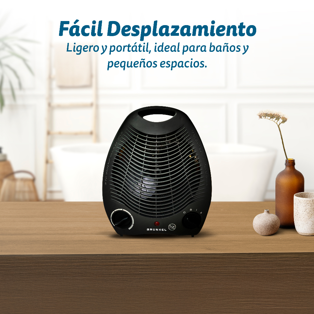 Un calefactor eléctrico negro sobre una mesa de madera. Un jarrón con flor, una piedra pequeña y una taza a la derecha. En el fondo, un baño.