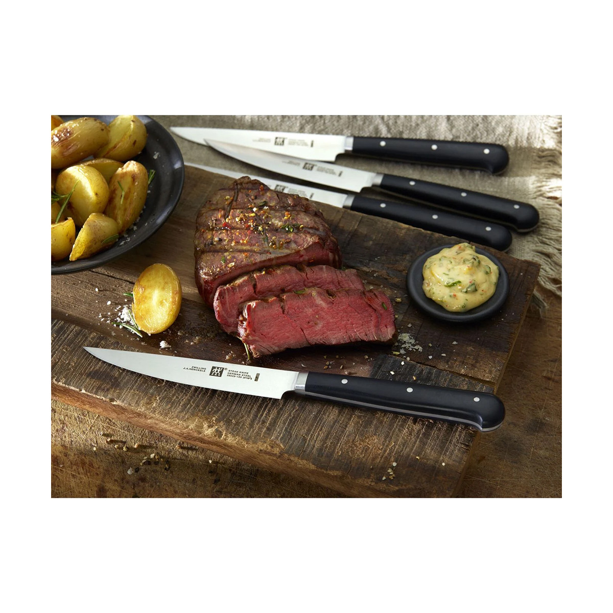 Stek z pokrojonymi porcjami, ziemniakami, sosem i nożami na drewnianej desce. Stek jest czerwony, a ziemniaki złote.