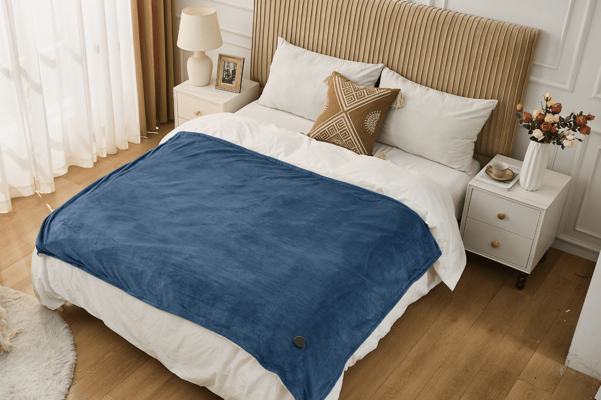 Schlafzimmer mit einem Bett, das mit einer blauen Decke bedeckt ist. Ein gemustertes Kissen und eine Blumenvase sind sichtbar.
