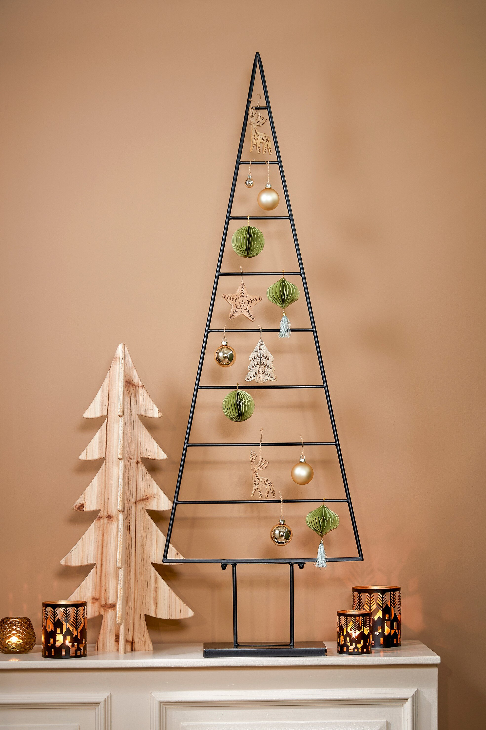 Décorations de Noël. Un arbre en métal, un arbre en bois, des ornements et des bougies sur une surface blanche contre un mur marron.